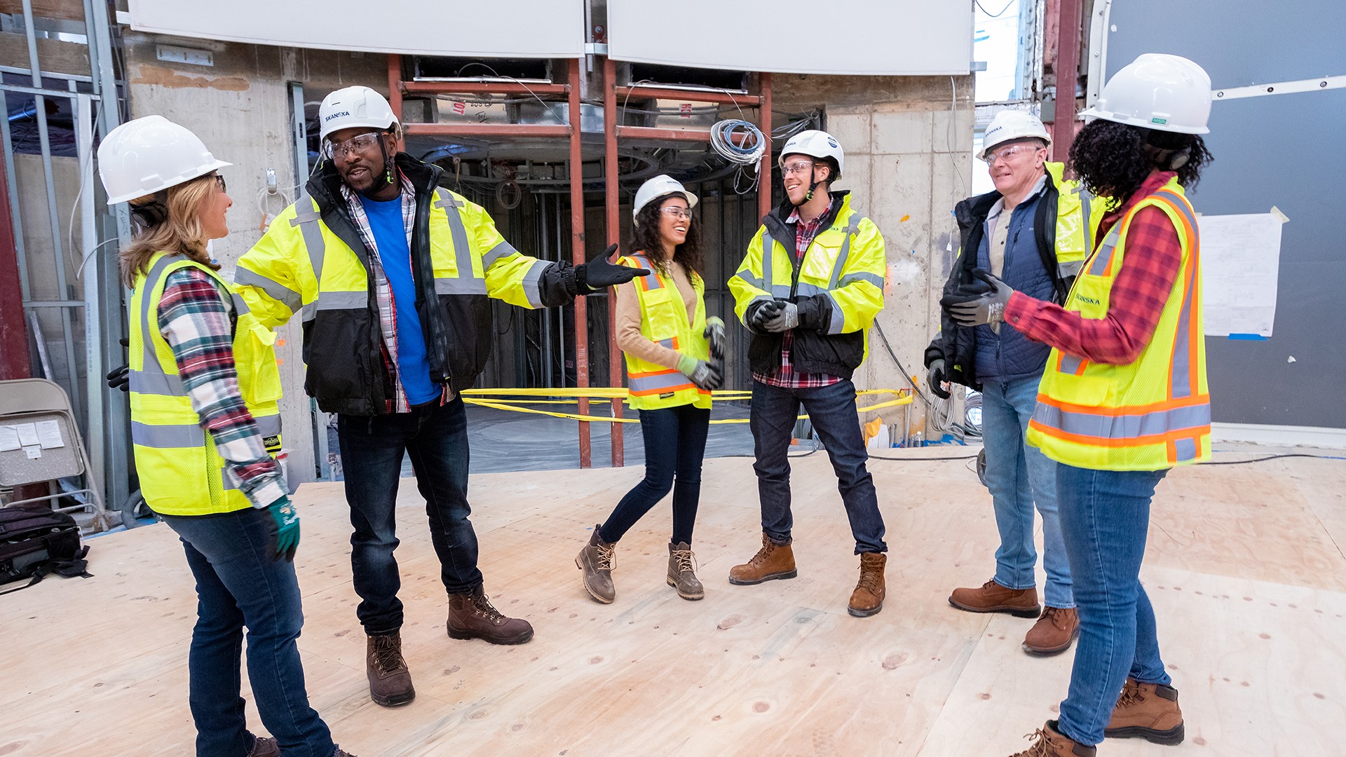 Construction Team Meeting on Site: Safety and Coordination Construction team in safety gear discussing plans at a building site.