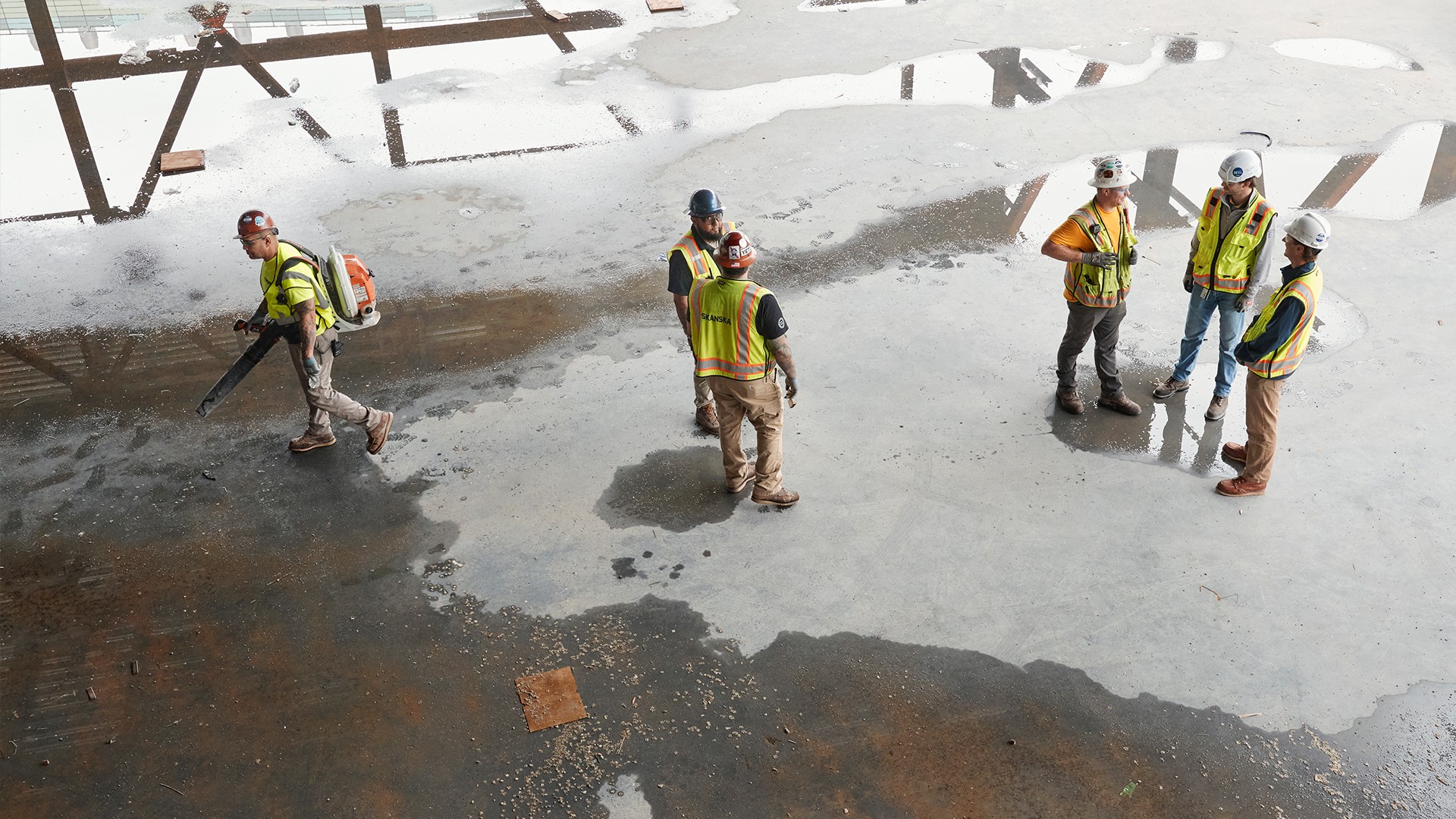 Construction workers in safety gear inspecting a wet concrete floor at a building site.