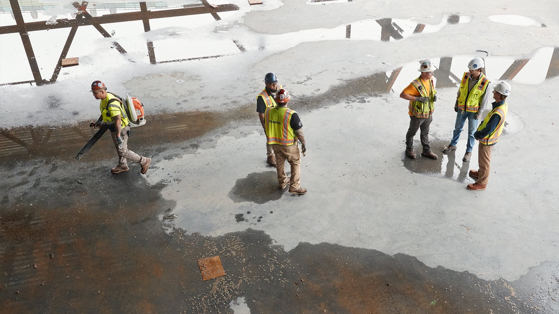 Construction workers in safety gear inspecting a wet concrete floor at a building site.