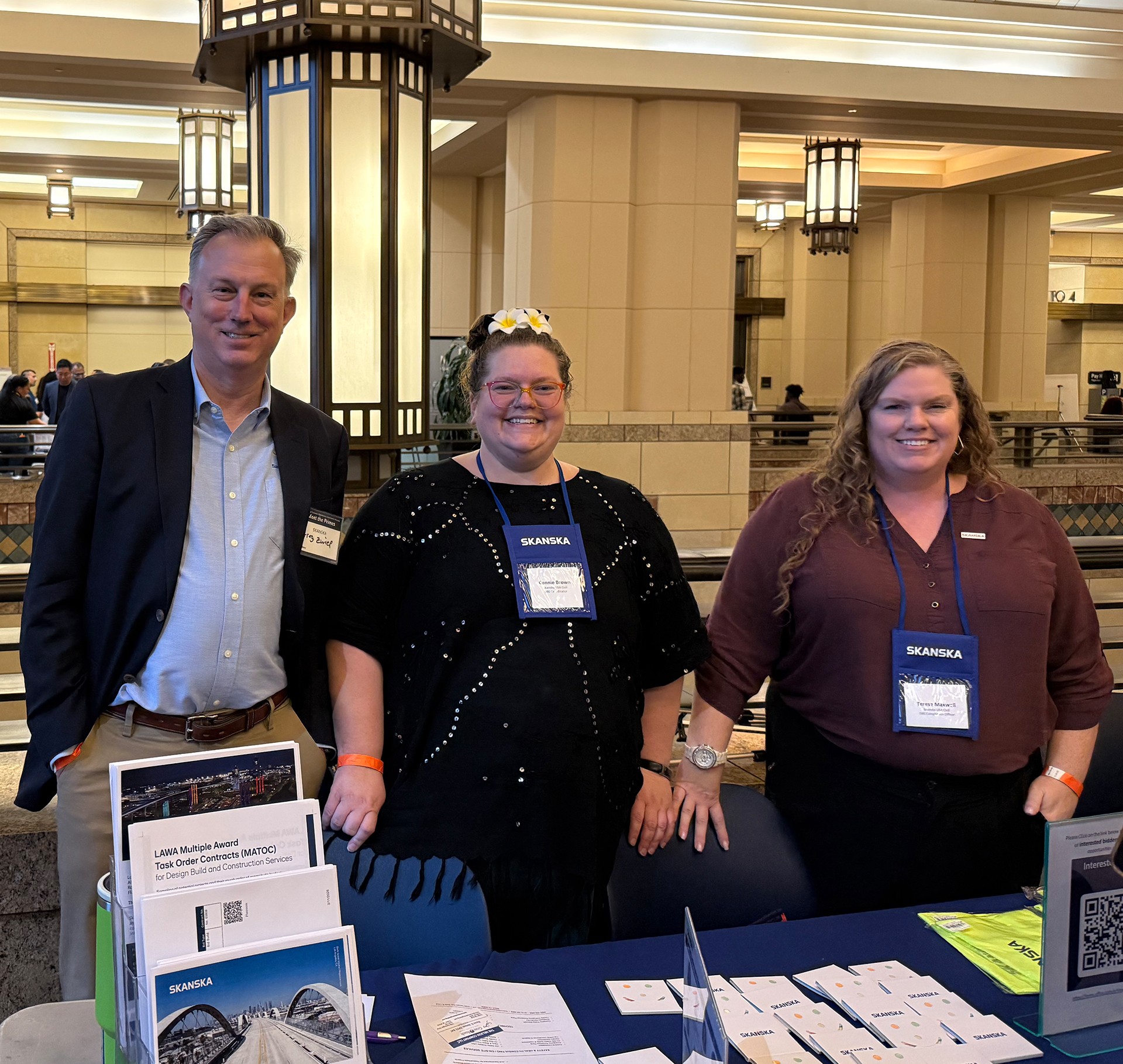 Skanska Team Networking at Industry Conference Booth Three professionals with Skanska badges at a conference table with brochures and flyers.