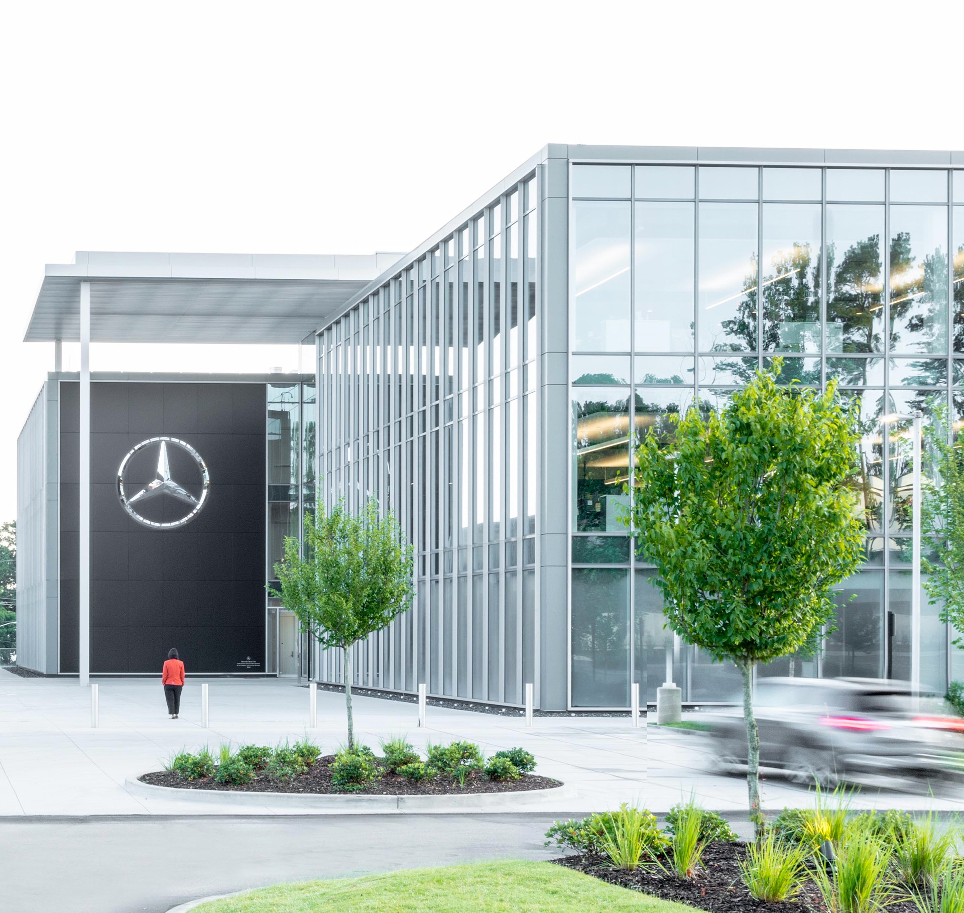 Modern glass building entrance with Mercedes-Benz logo, featuring sleek architectural design.