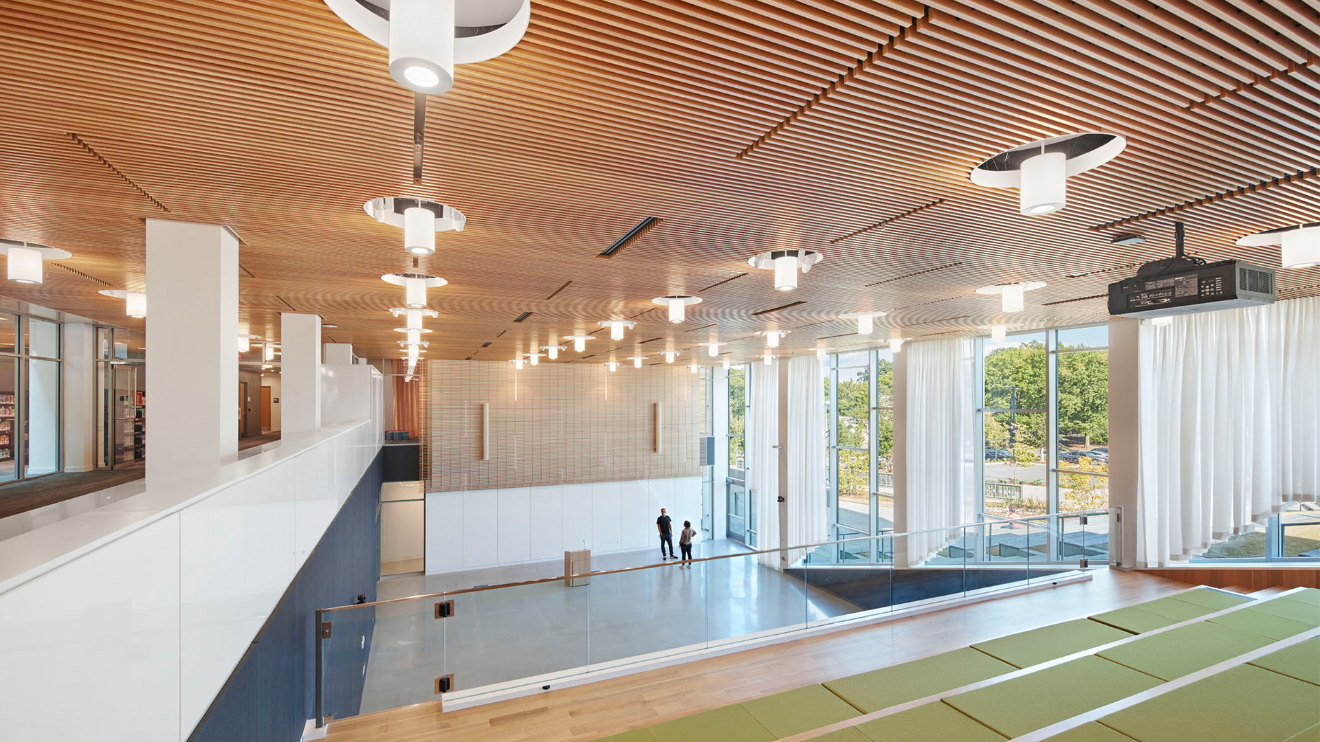 Modern auditorium with wooden ceiling, tiered seating, and large windows overlooking greenery.