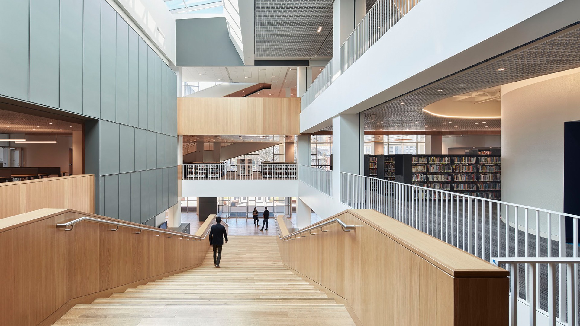 Modern library interior with wooden stairs, bookshelves, and natural lighting.