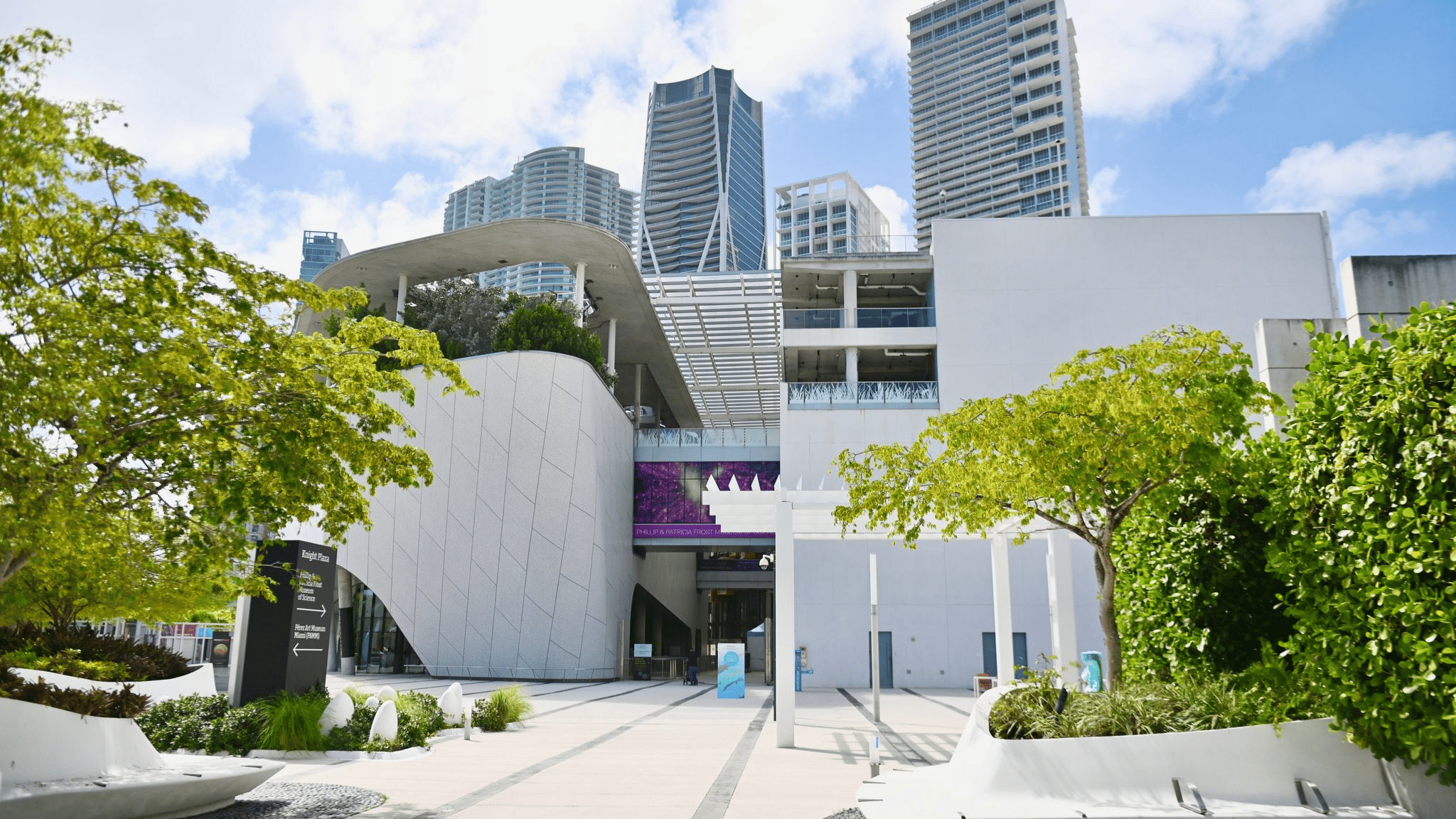Modern urban building entrance with greenery and skyscrapers in the background.