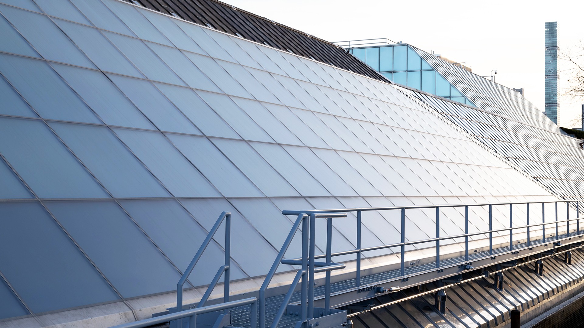 Modern glass building facade with metal railing and geometric panel design in daylight.