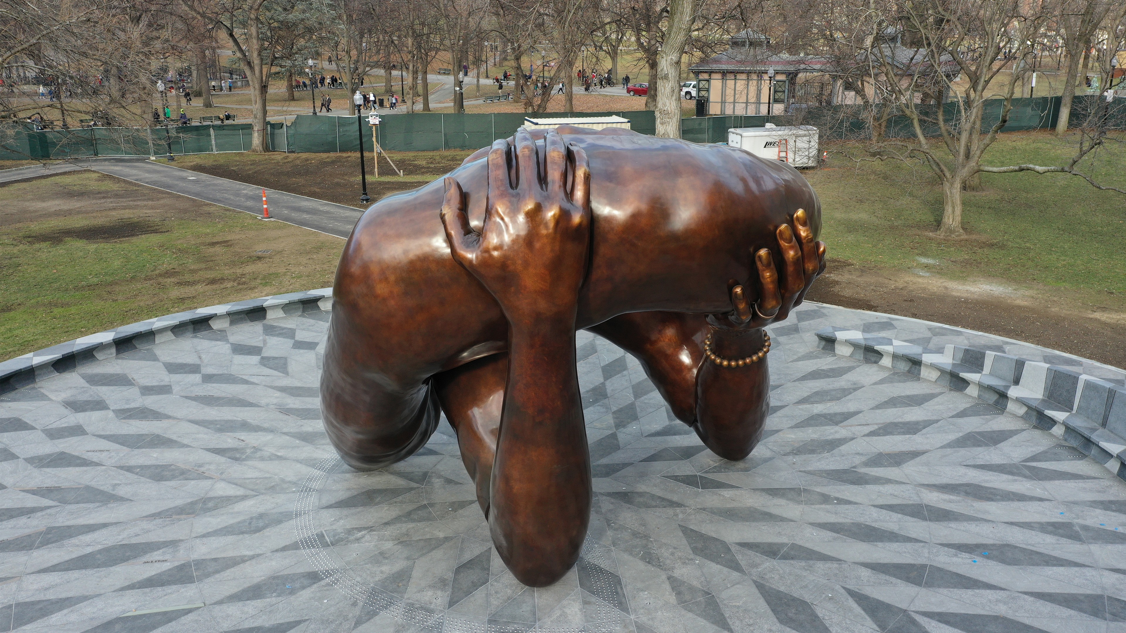 Bronze sculpture of a person curled up, holding their head, displayed outdoors.