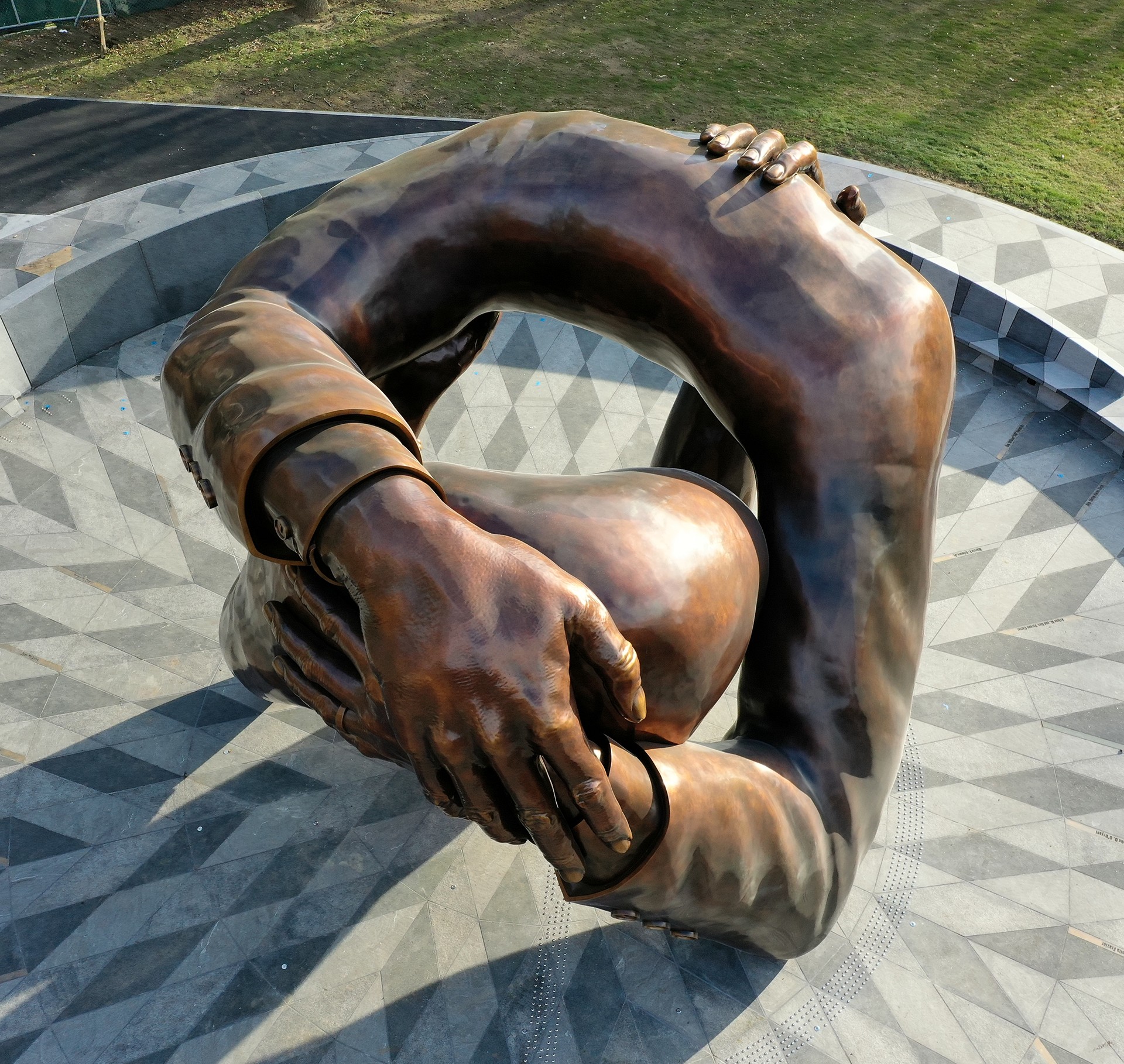 Bronze Sculpture of Intertwined Arms Embracing in Outdoor Park Bronze sculpture of intertwined arms and hands forming a continuous loop outdoors.