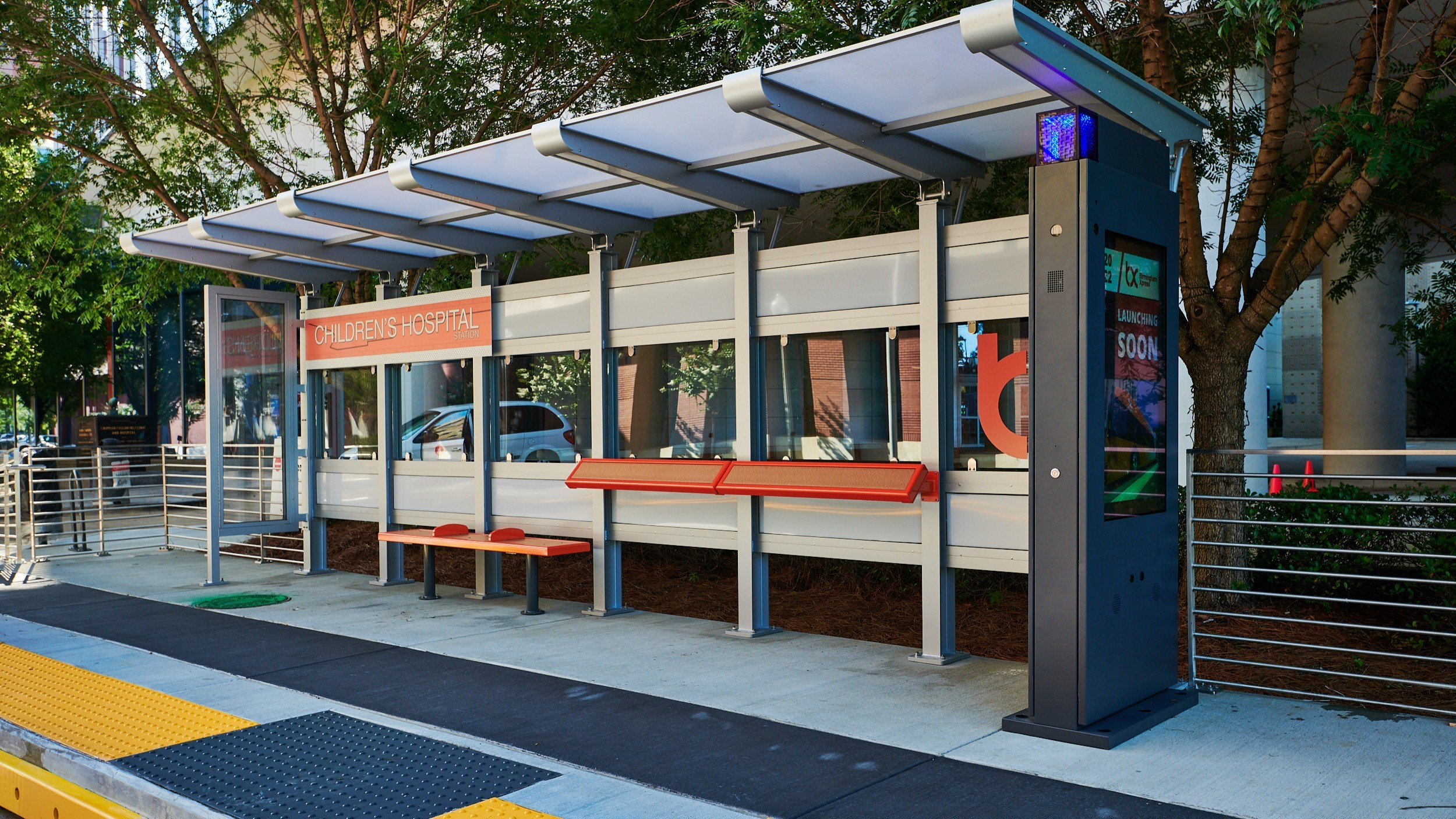 Modern bus stop shelter with clear panels and benches near Children's Hospital.