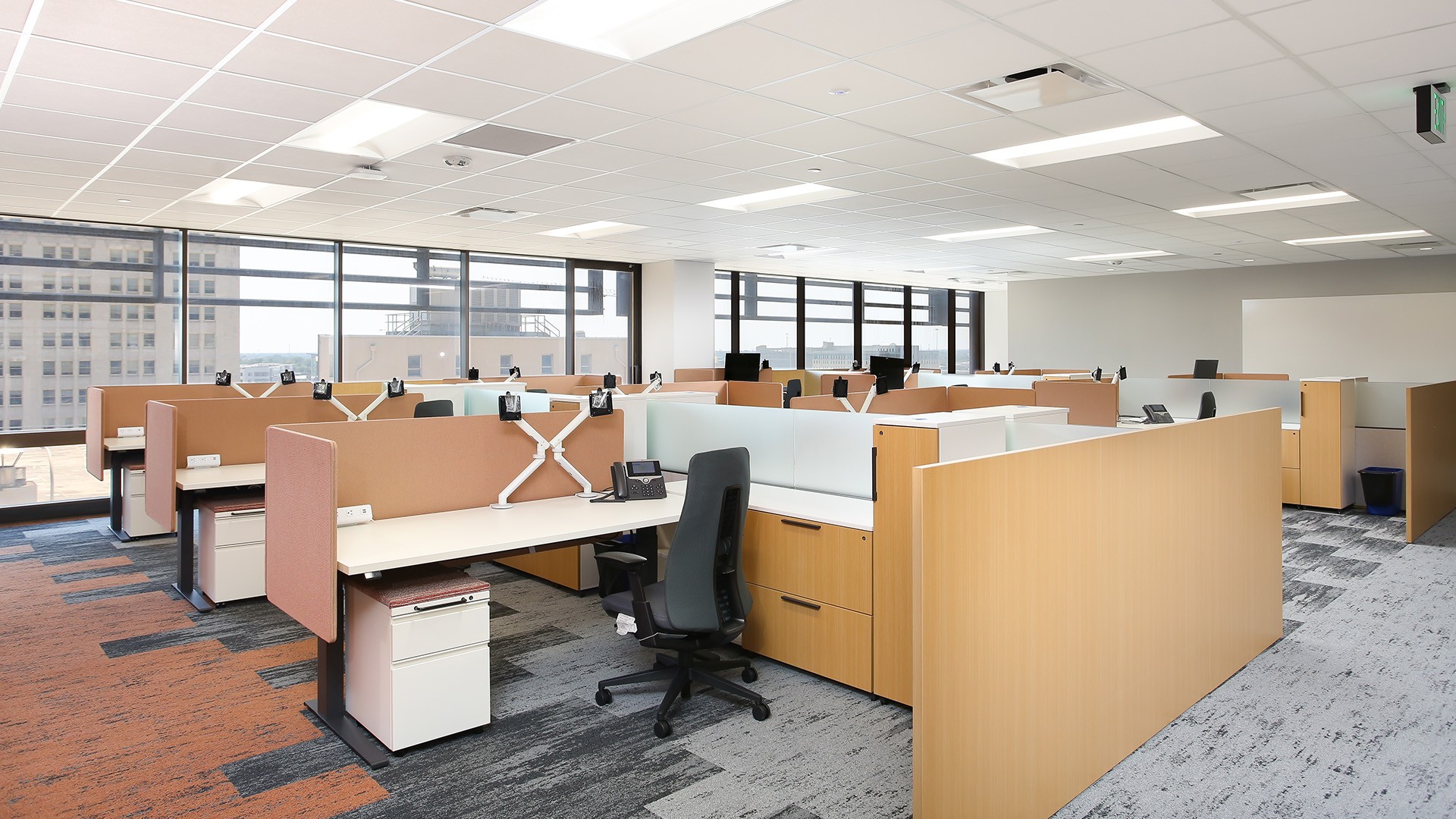 Modern office workspace with cubicles, ergonomic chairs, and large windows.