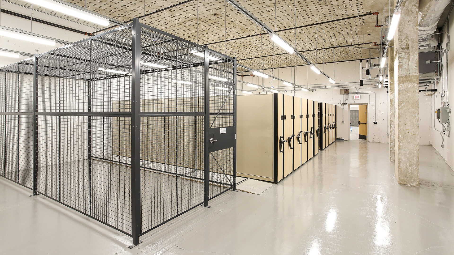 Secure storage room with metal cages and beige filing cabinets in a clean industrial space.