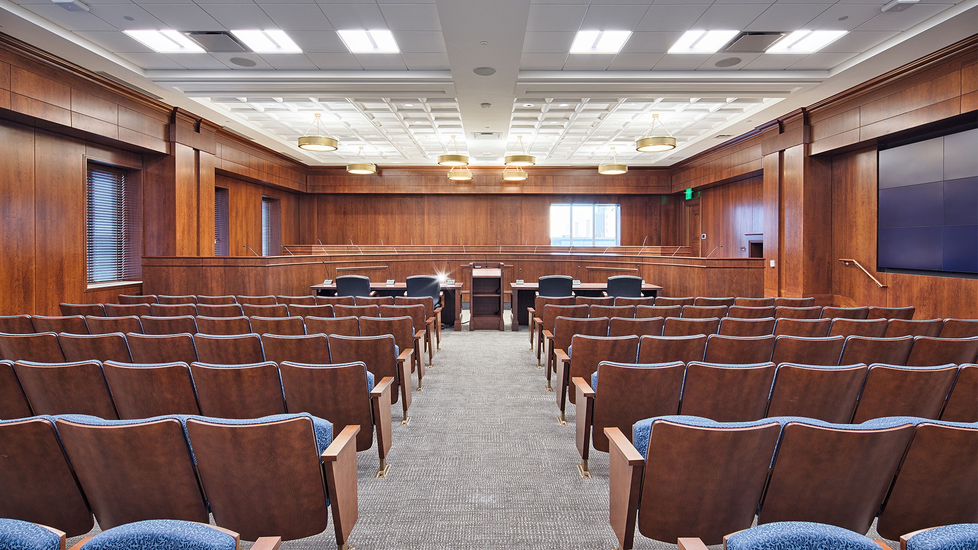 Modern courtroom interior with wooden paneling, seating, and judge's bench.