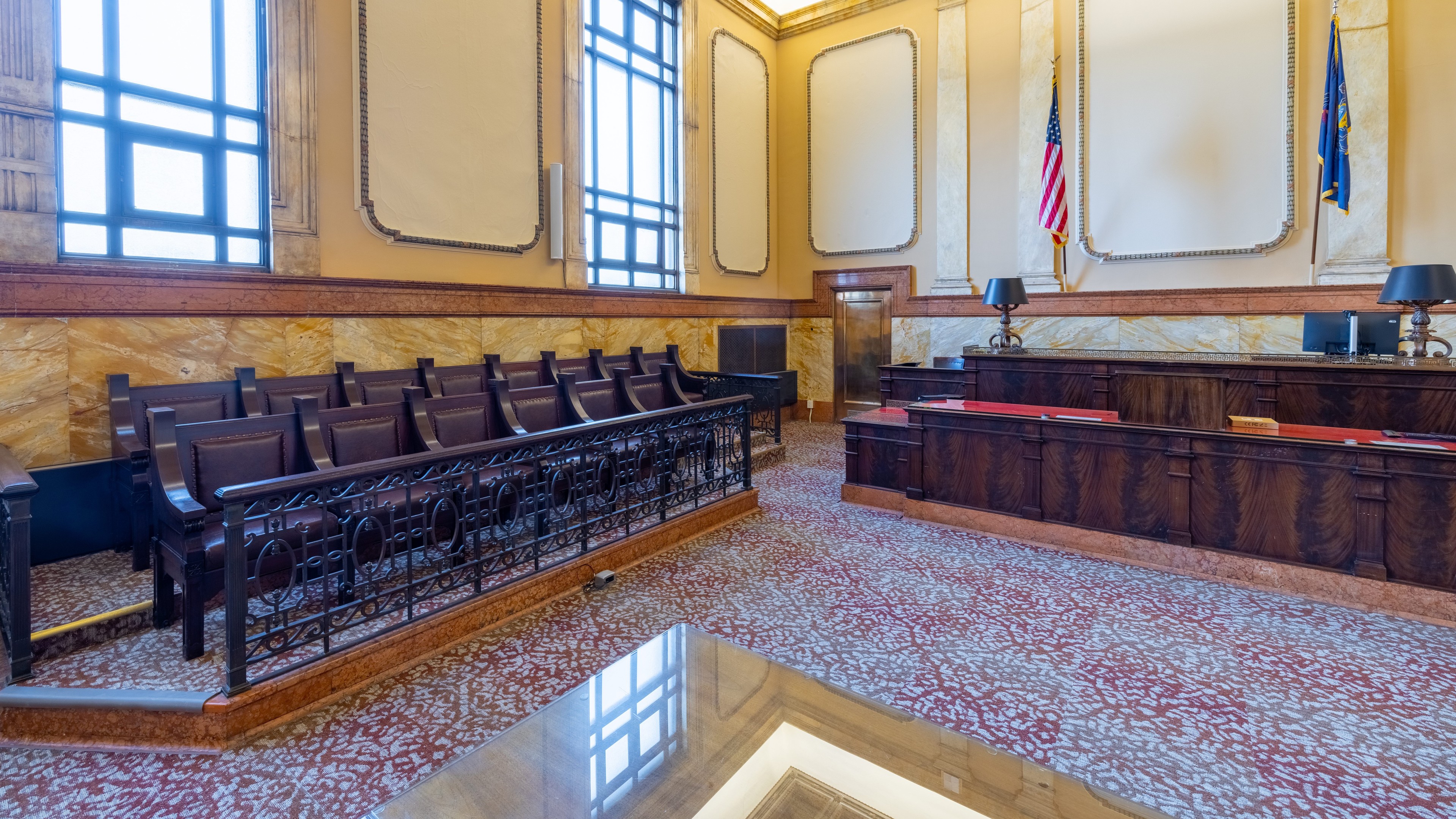 Interior of a historic courtroom with wooden benches, judge’s bench, and American flags.