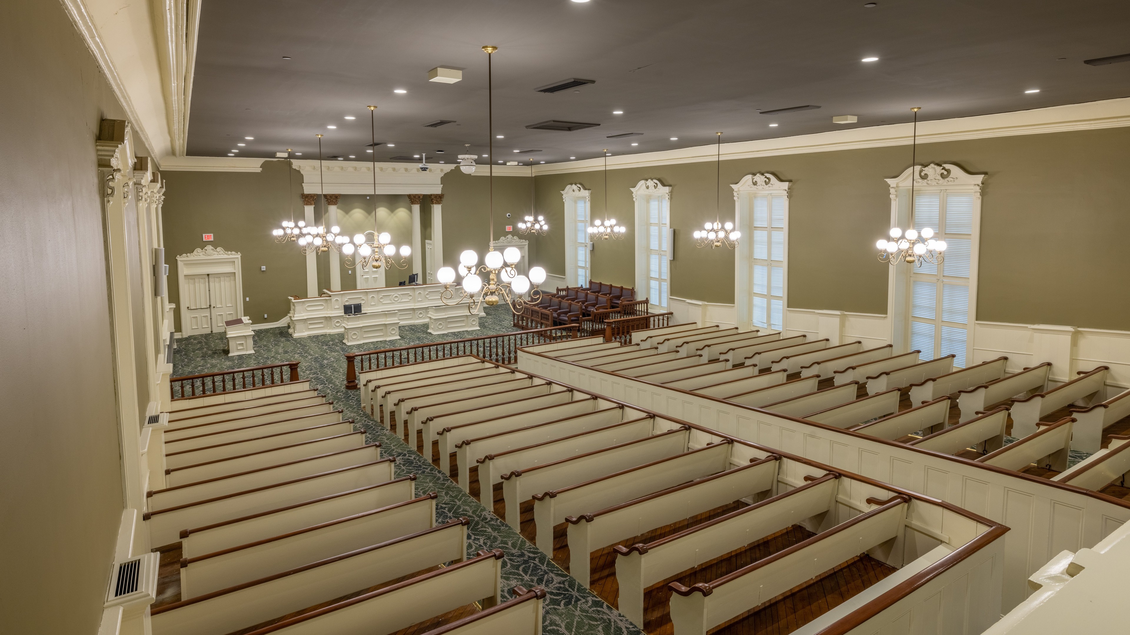 Interior view of a spacious, historic courtroom with wooden benches and chandeliers.