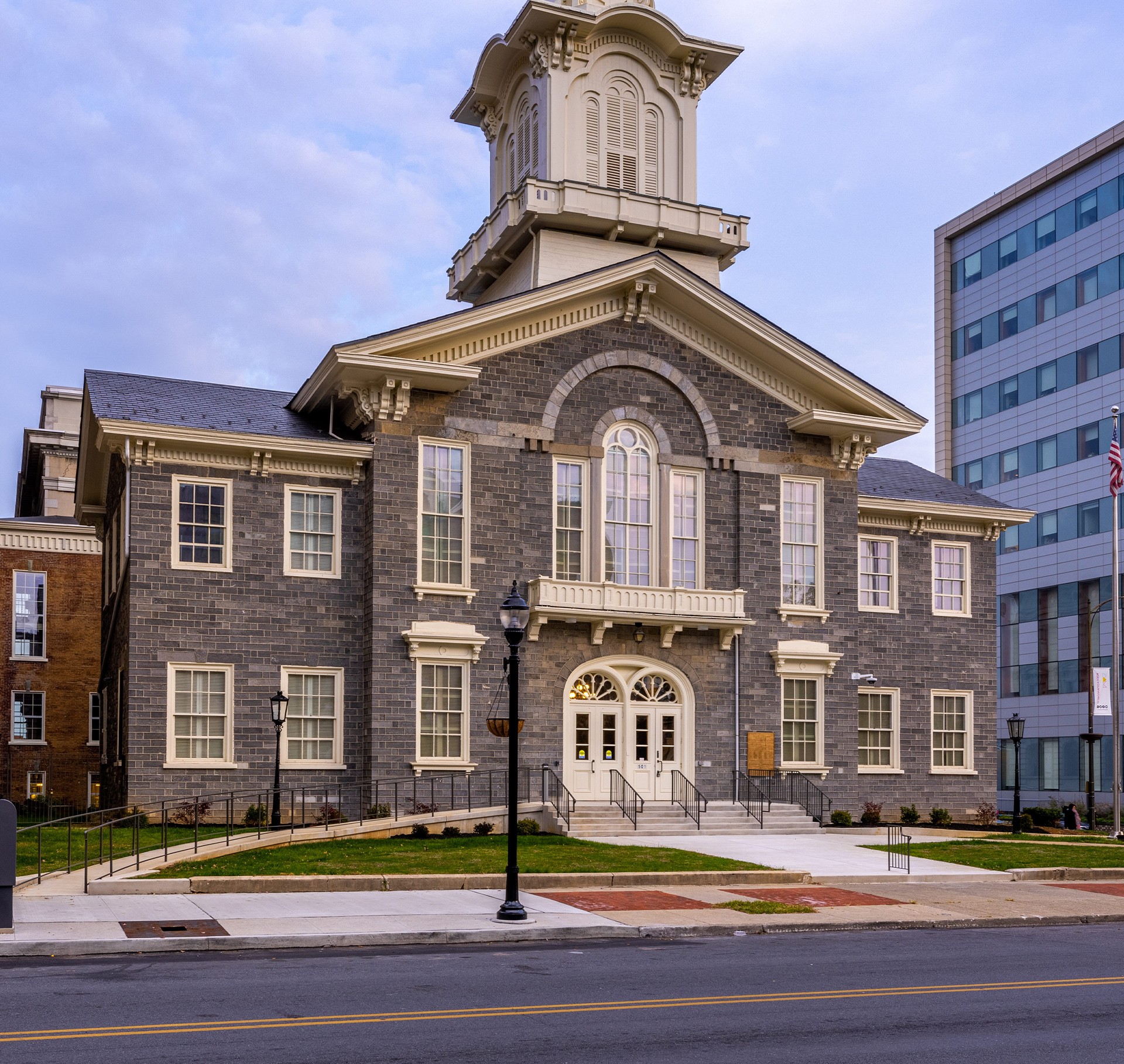 Historic courthouse building with modern office nearby at dusk Historic gray brick courthouse with white trim and a clock tower under a blue sky.
