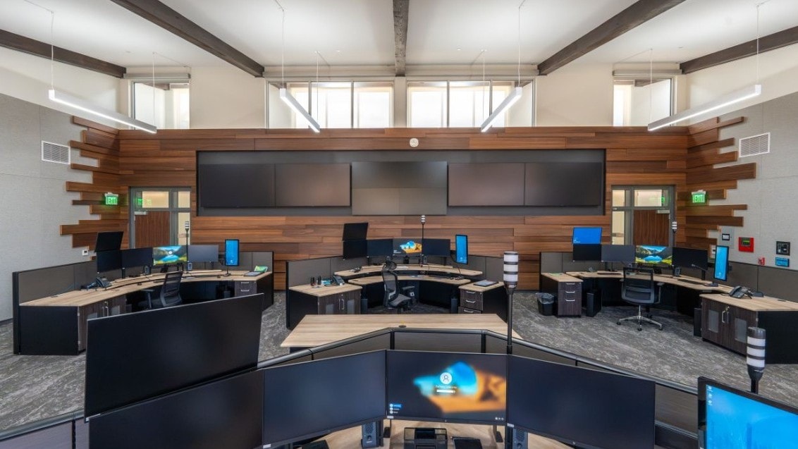 Modern control room with multiple monitors, ergonomic chairs, and wood-paneled walls.