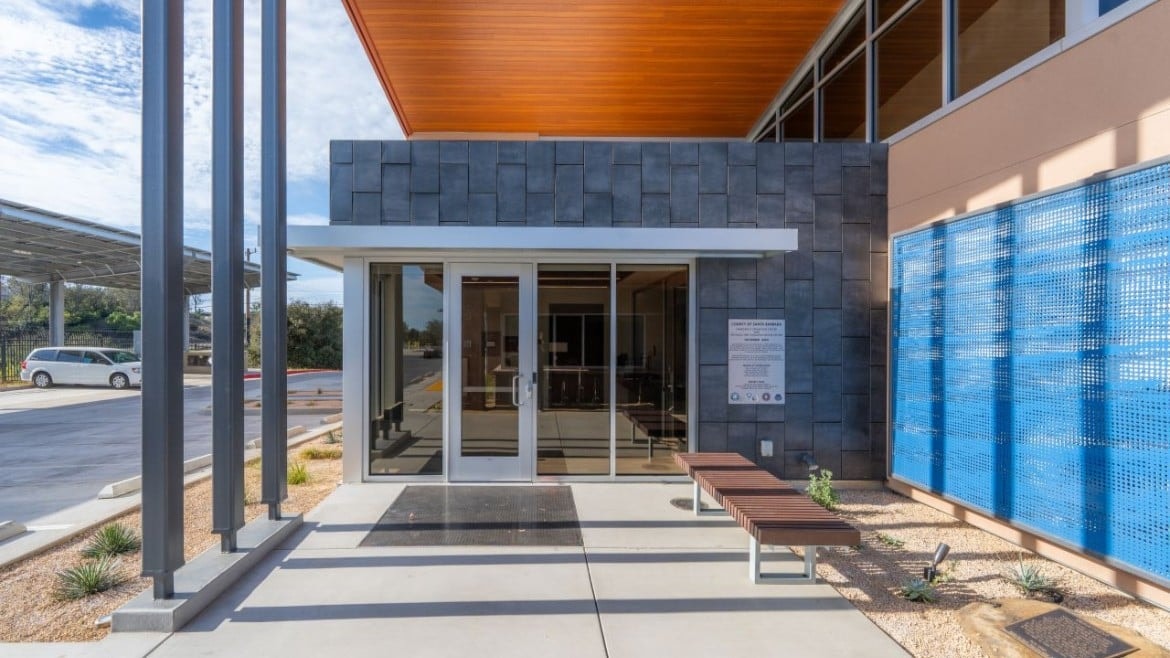 Modern building entrance with glass doors, benches, and a blue perforated wall panel.