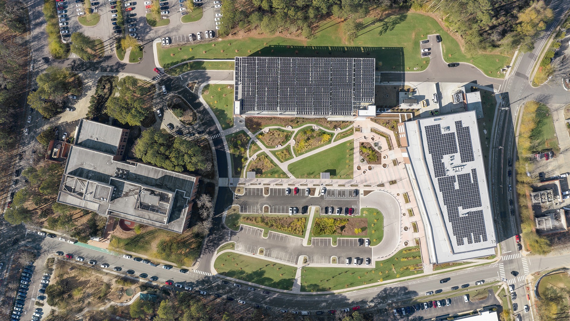 Aerial view of a solar panel-covered building complex with parking and greenery.