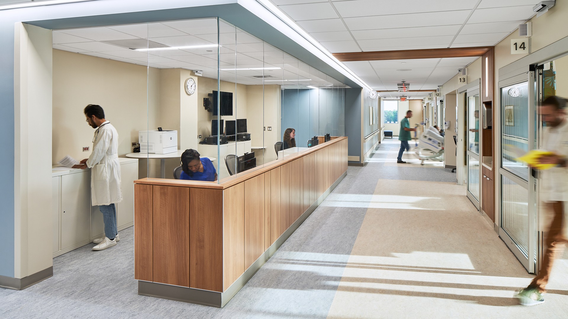 Hospital corridor with staff at reception and medical personnel moving in the hallway.