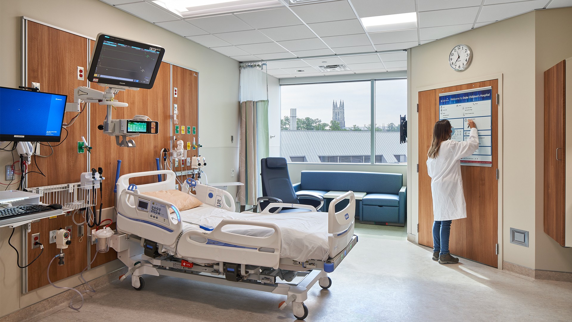 Modern hospital room with medical equipment, bed, and a doctor writing on a board.