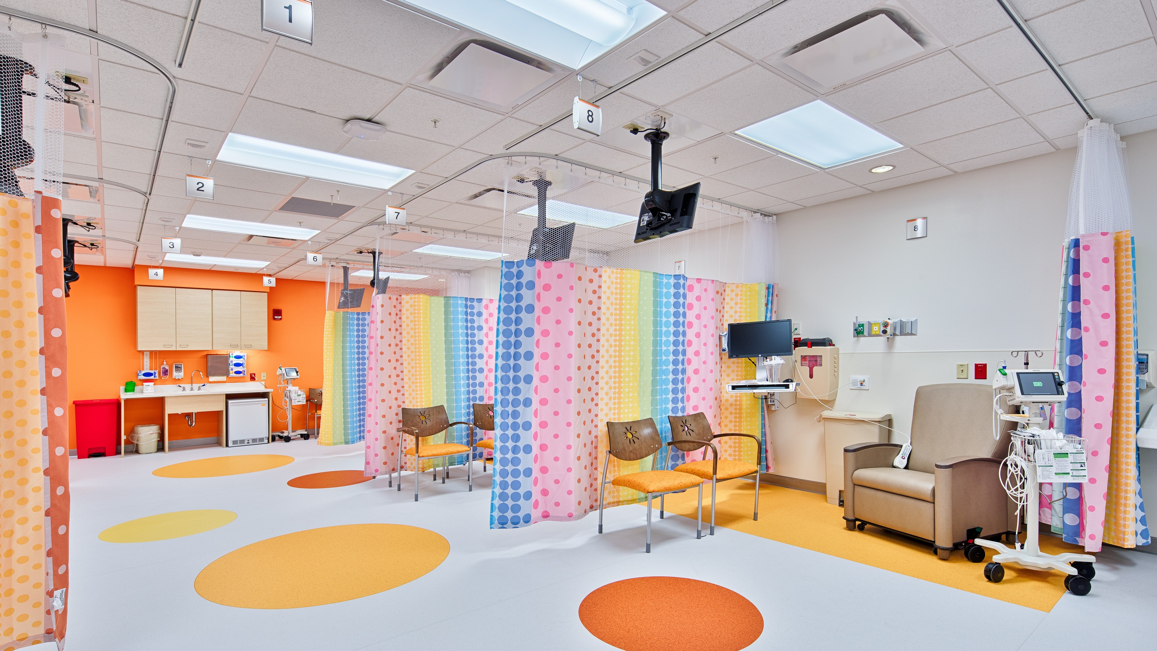 Bright pediatric hospital room with colorful curtains, chairs, and medical equipment.