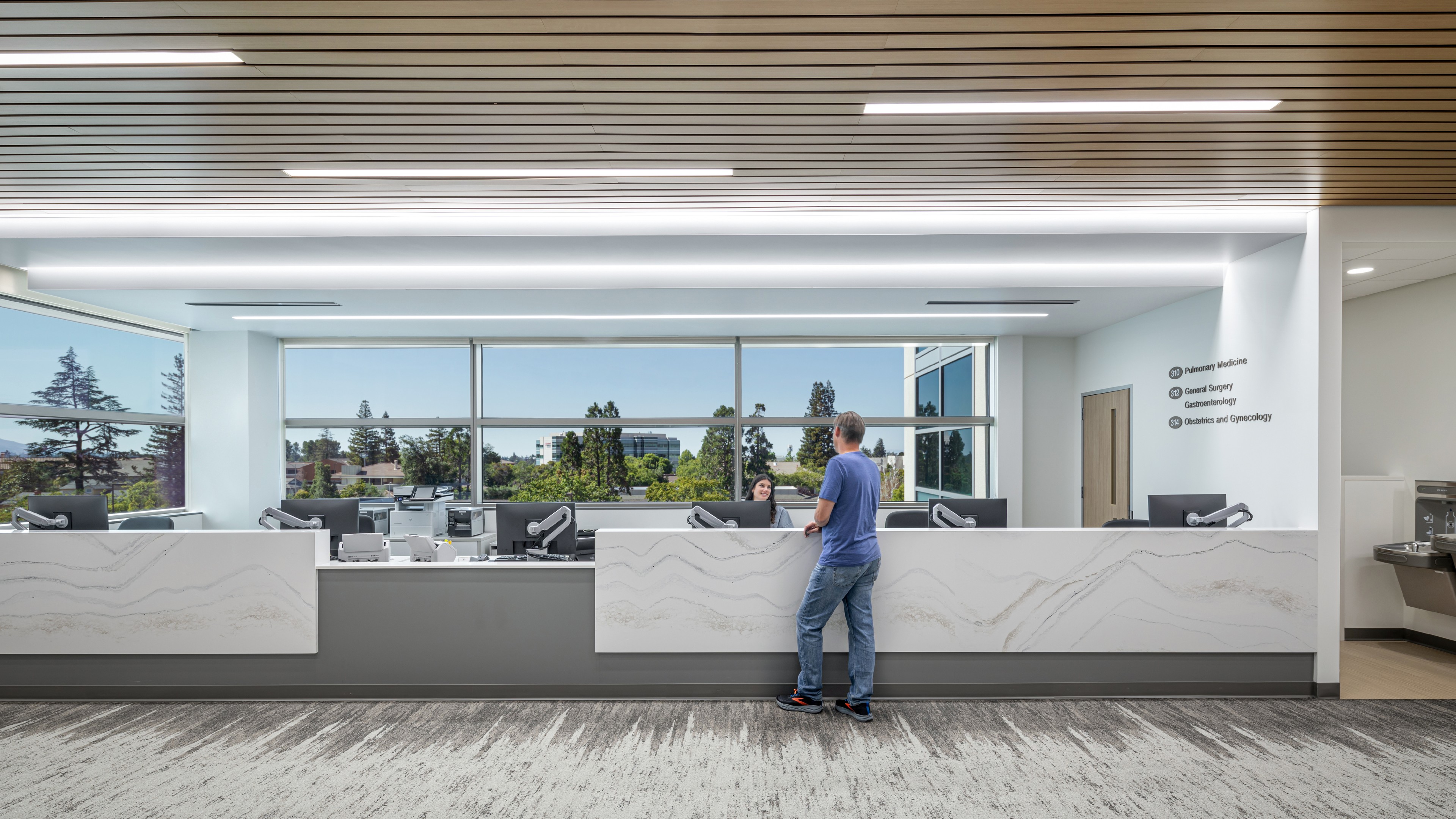 Modern Medical Reception Area with Patient and Staff Interaction Modern medical reception area with a visitor speaking to a staff member behind the counter.