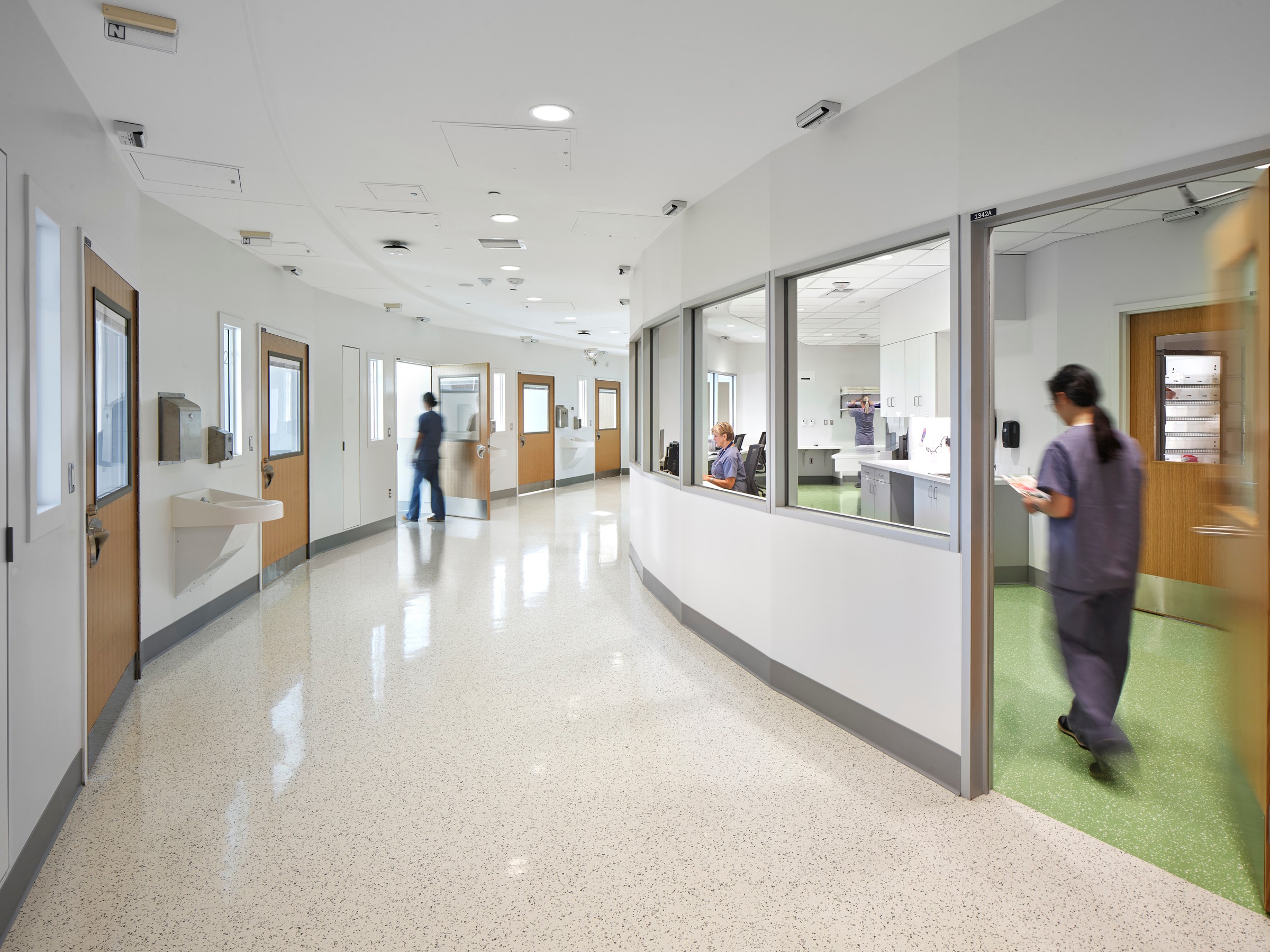 Moderno corredor de hospital con personal médico en uniforme, diseño limpio y iluminación brillante.