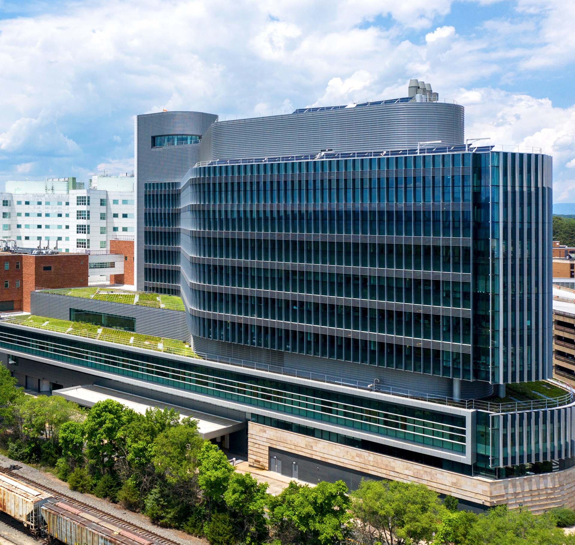 Modern building with glass facade and rooftop greenery under a partly cloudy sky.