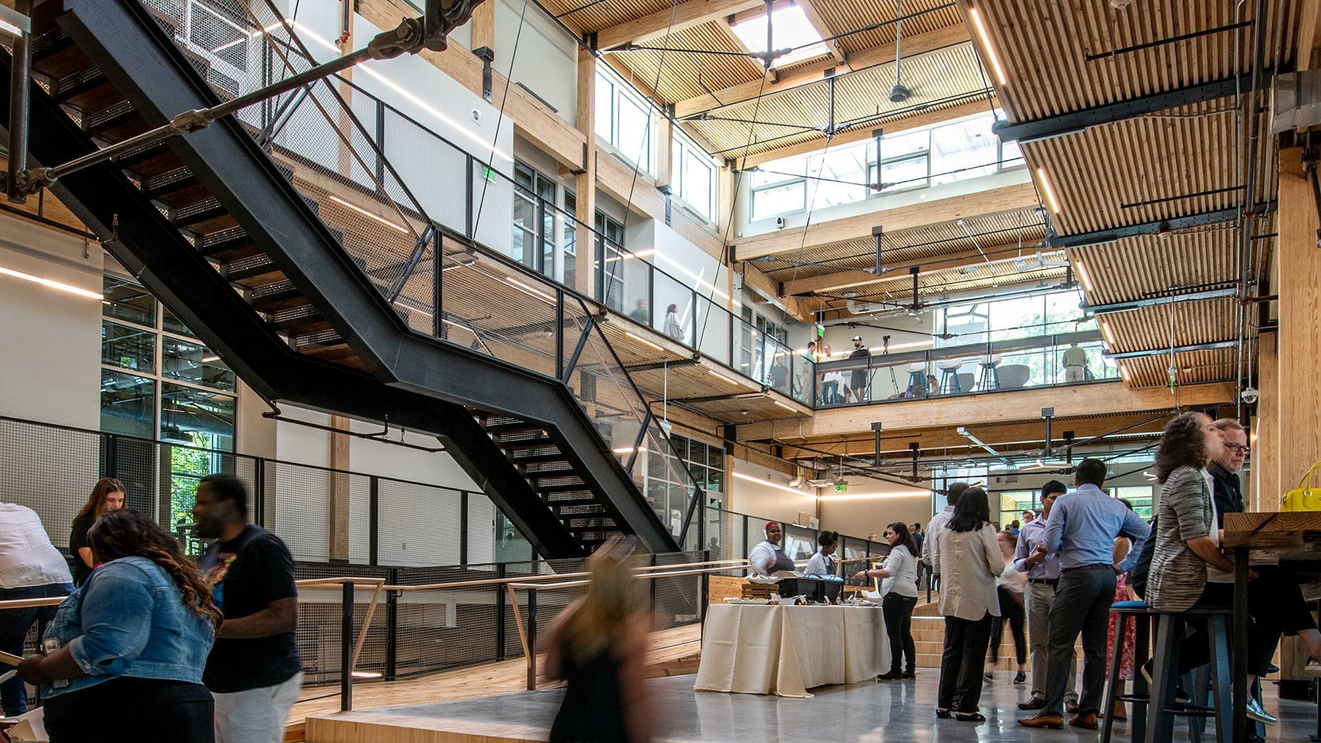 Modern office interior with people socializing near a staircase and workspaces.