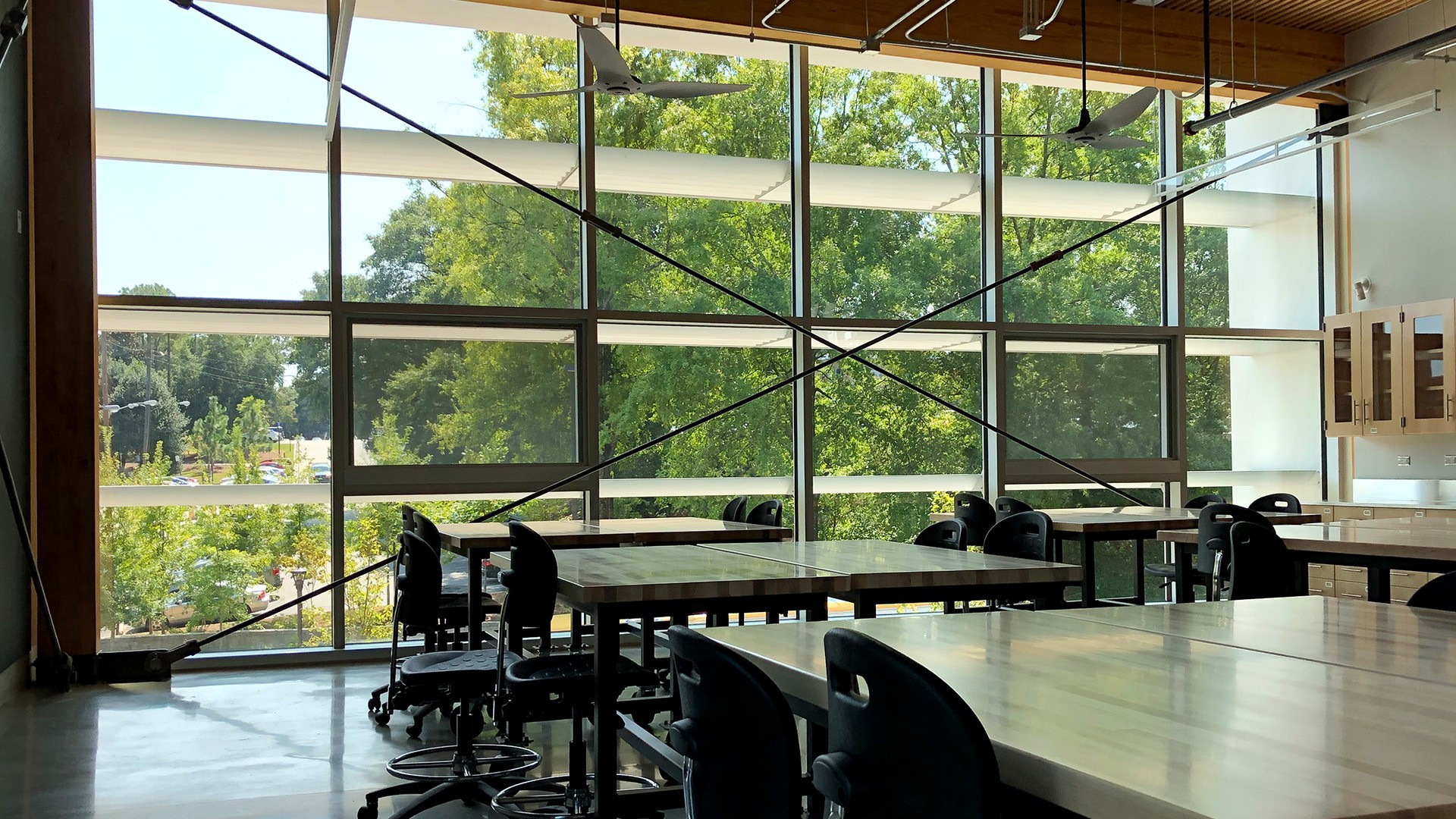 Modern classroom with large windows, natural light, and empty desks and chairs.