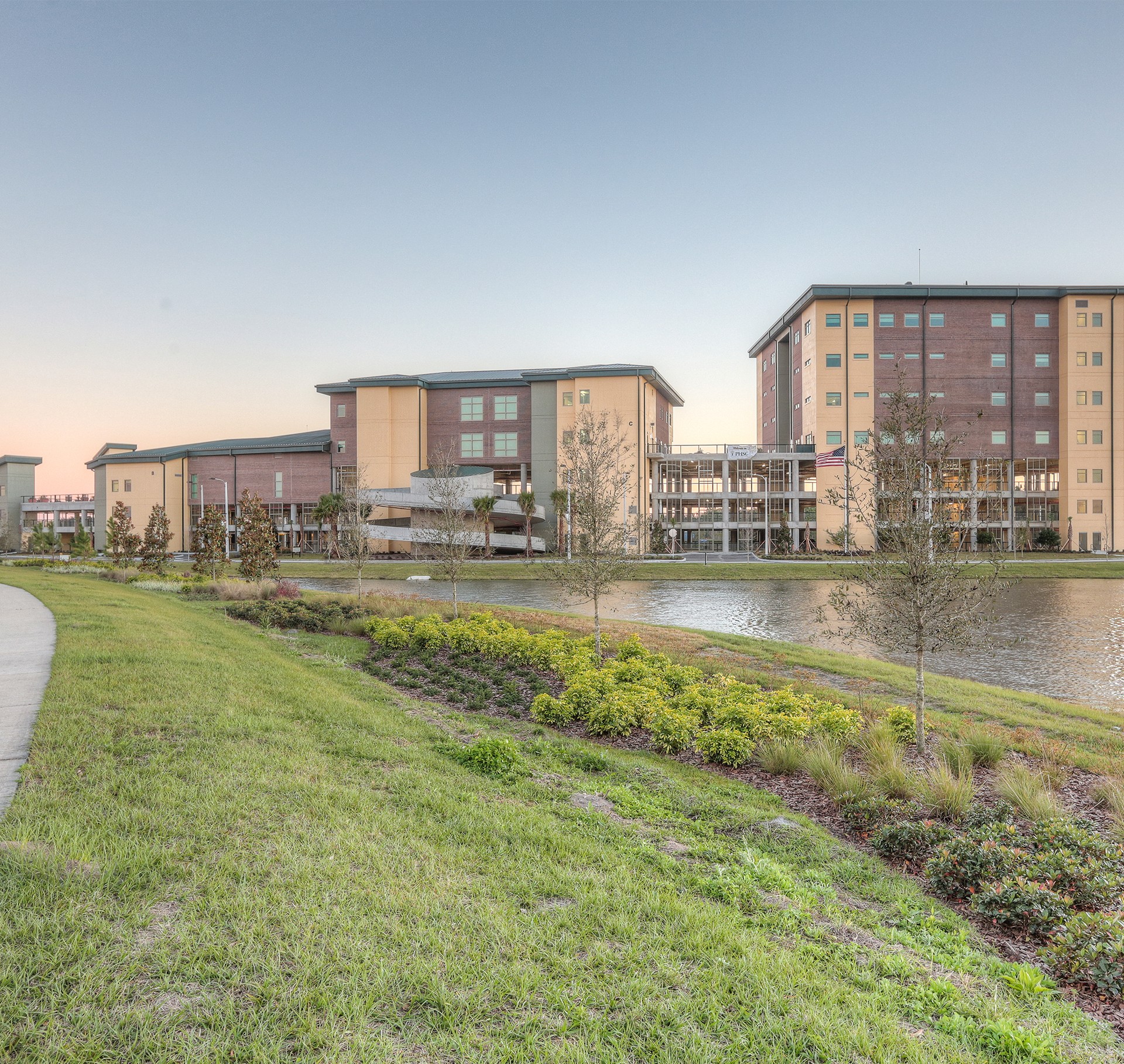 Modern Campus Buildings by Serene Lakeside at Sunset Modern buildings by a tranquil pond with landscaped greenery and a clear blue sky in the background.