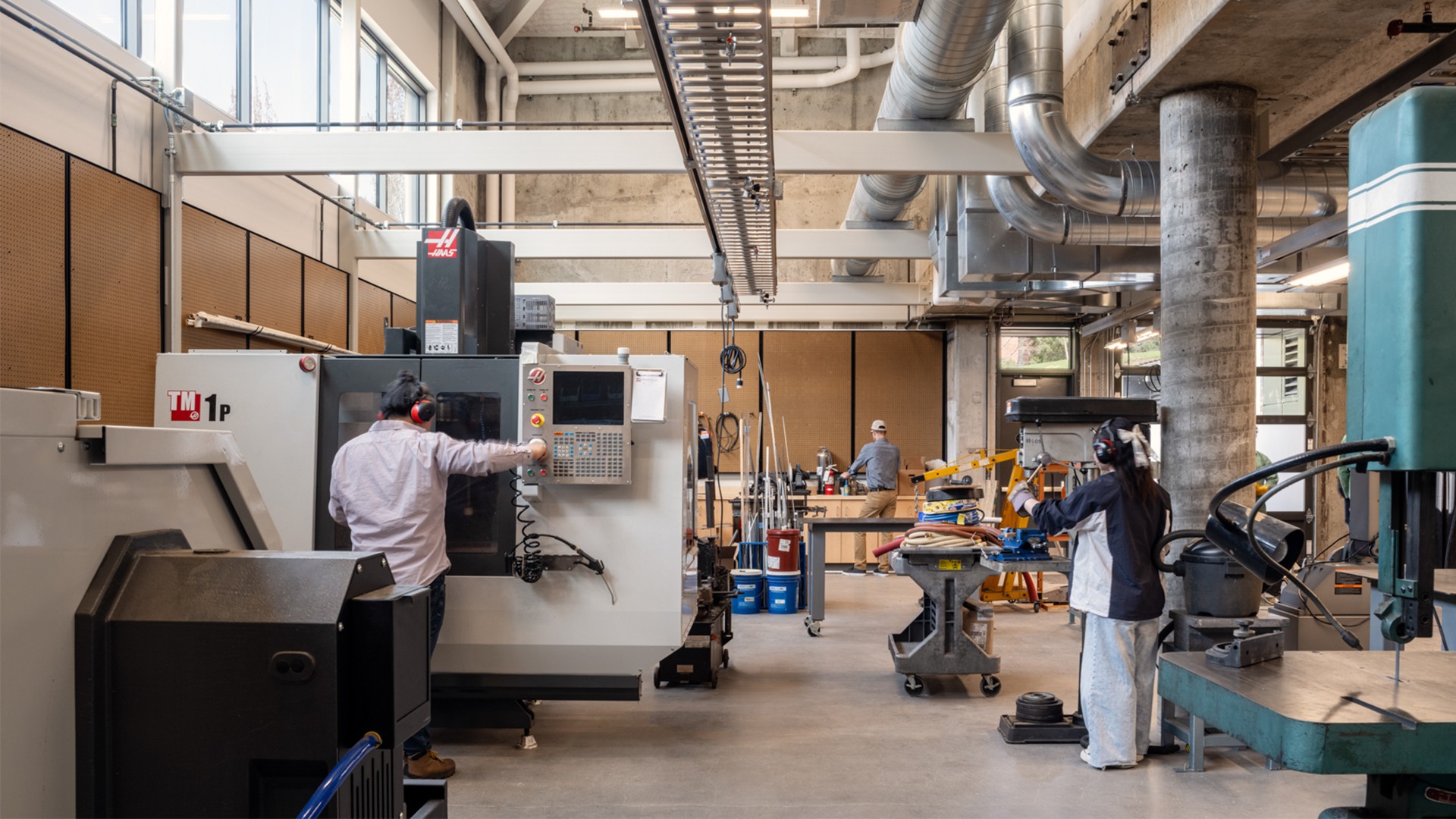 Industrial workers operating CNC machines in a spacious, well-lit manufacturing workshop.