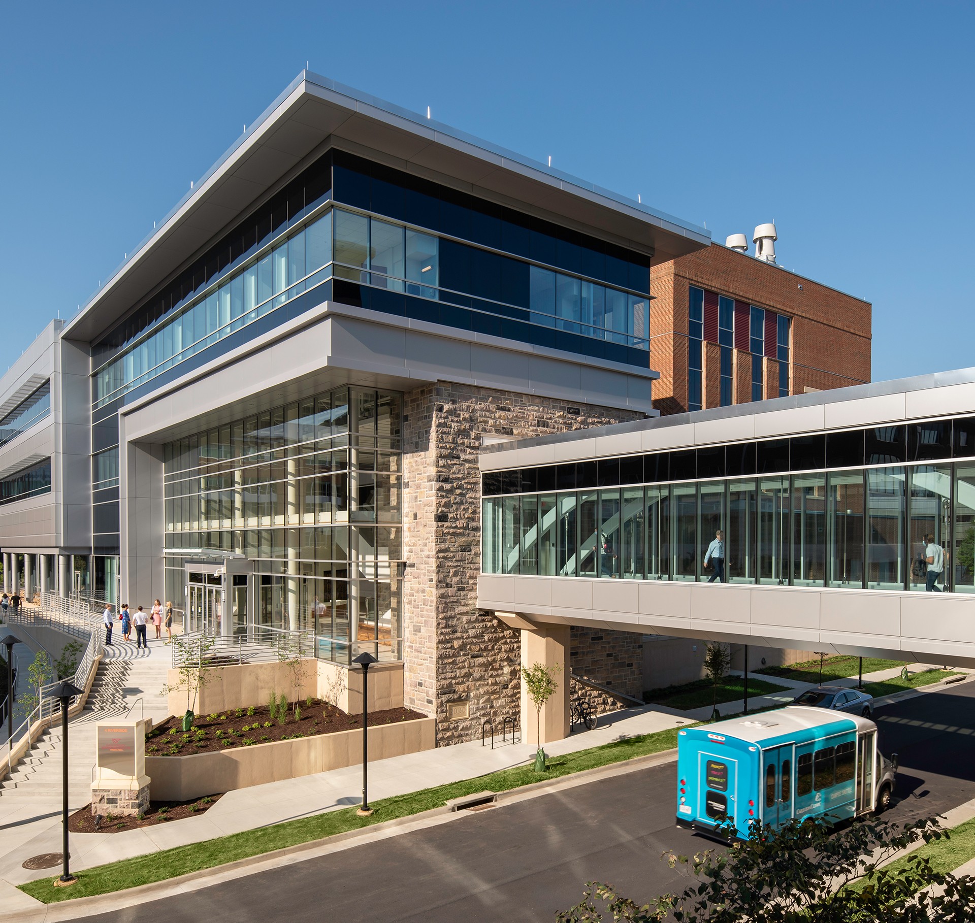 Modern Hospital Building with Glass Facade and Skywalk Bridge Modern office building with glass windows, sky bridge, and a blue shuttle bus outside.