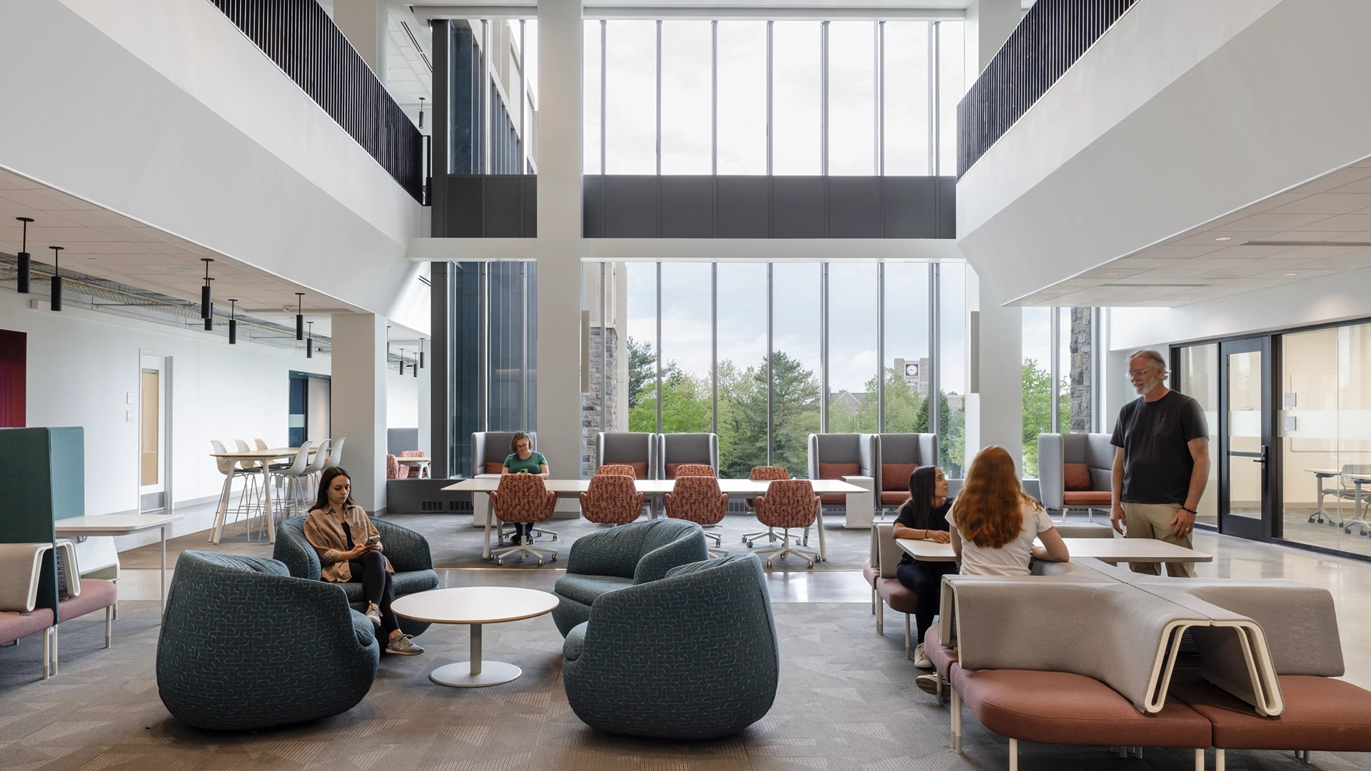 Modern office lounge with large windows, seating areas, and people collaborating.