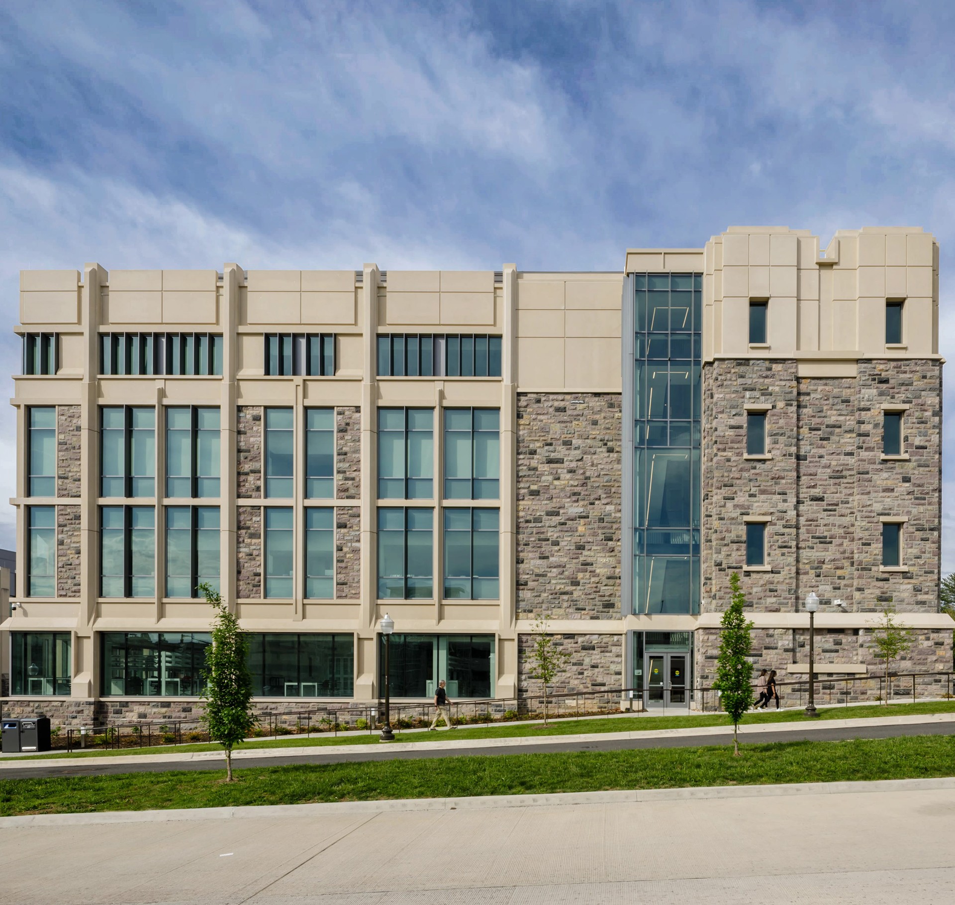 Modern university building with large windows and stone facade under a blue sky.