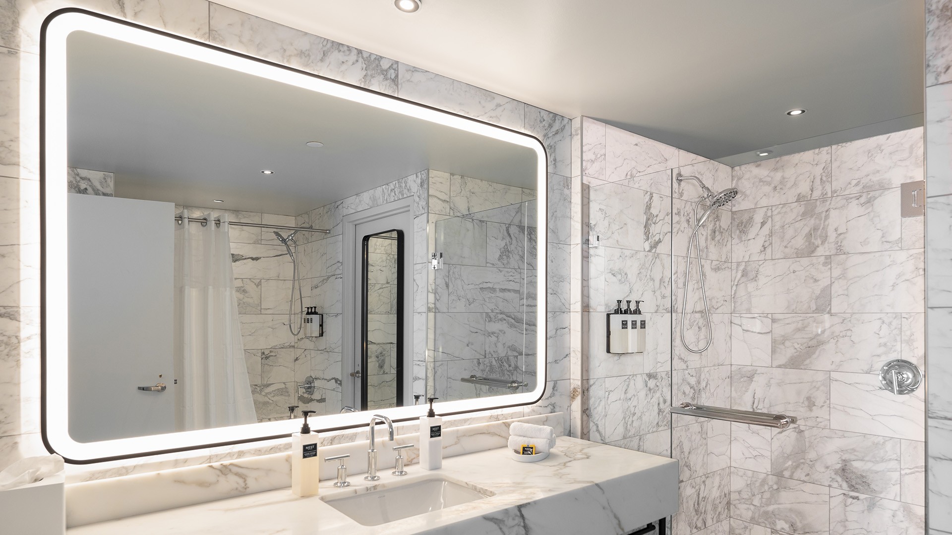 Modern bathroom with marble walls, illuminated mirror, and sleek sink area.