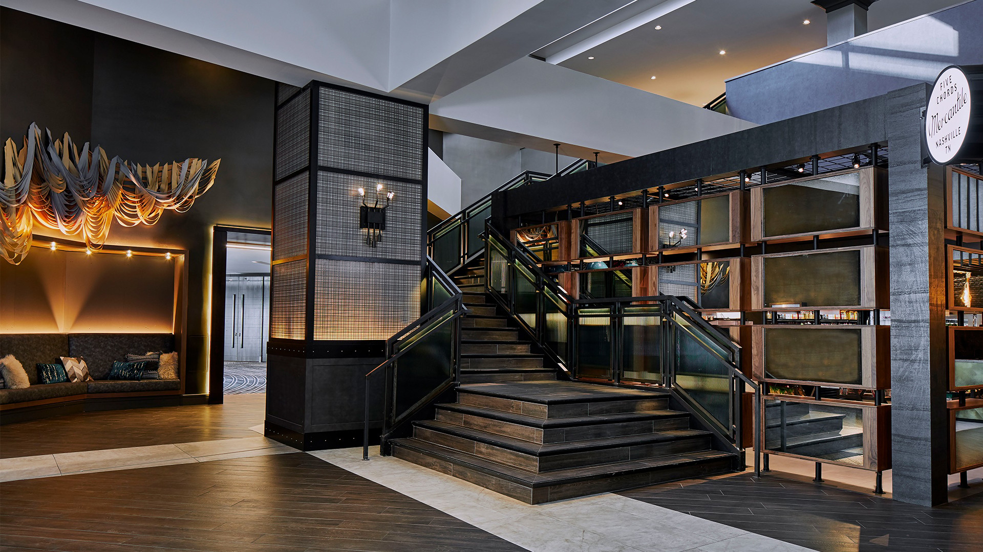 Modern hotel lobby with wooden stairs, cozy seating, and stylish lighting fixtures.