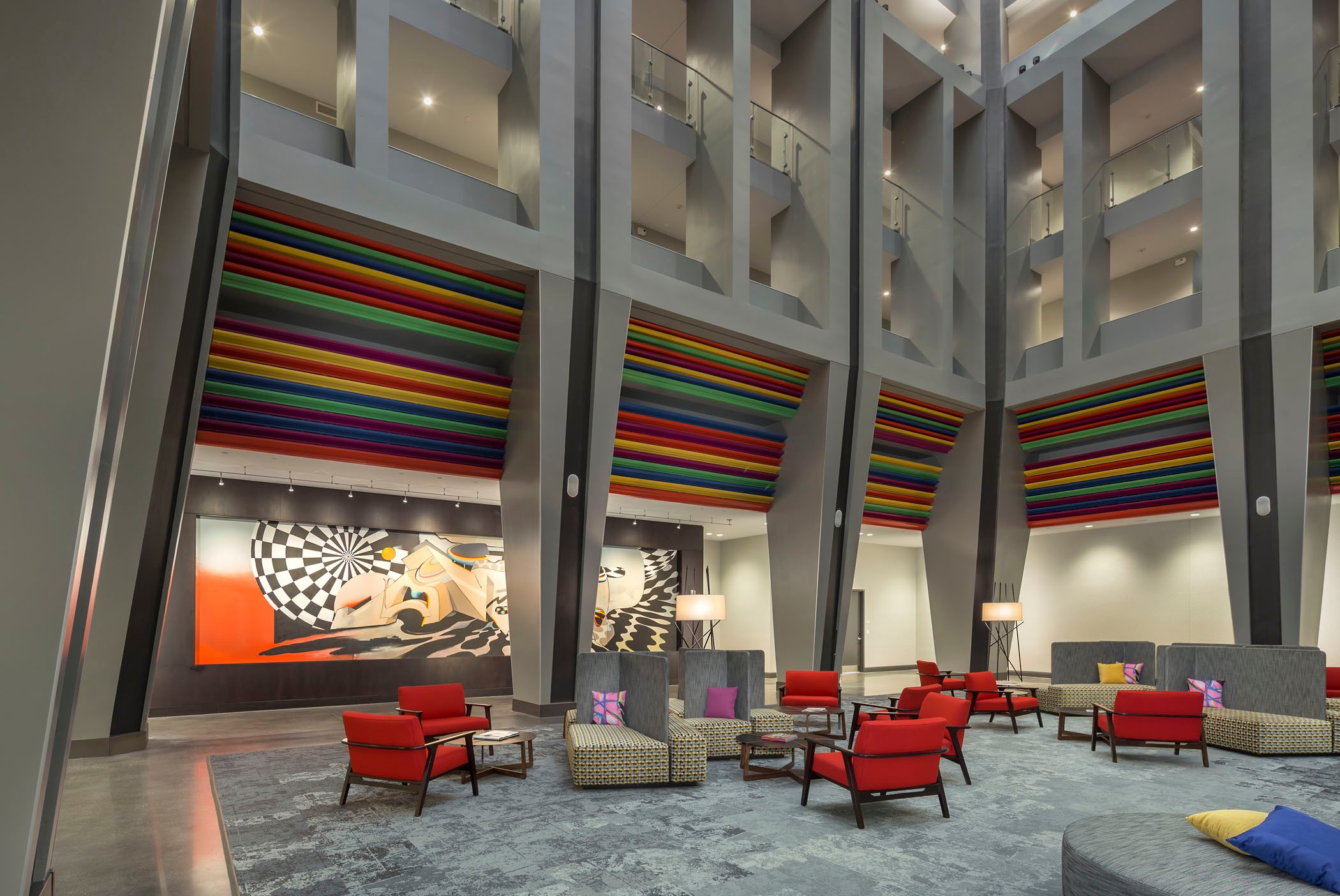 Modern lobby with colorful striped walls, abstract mural, red chairs, and geometric decor.