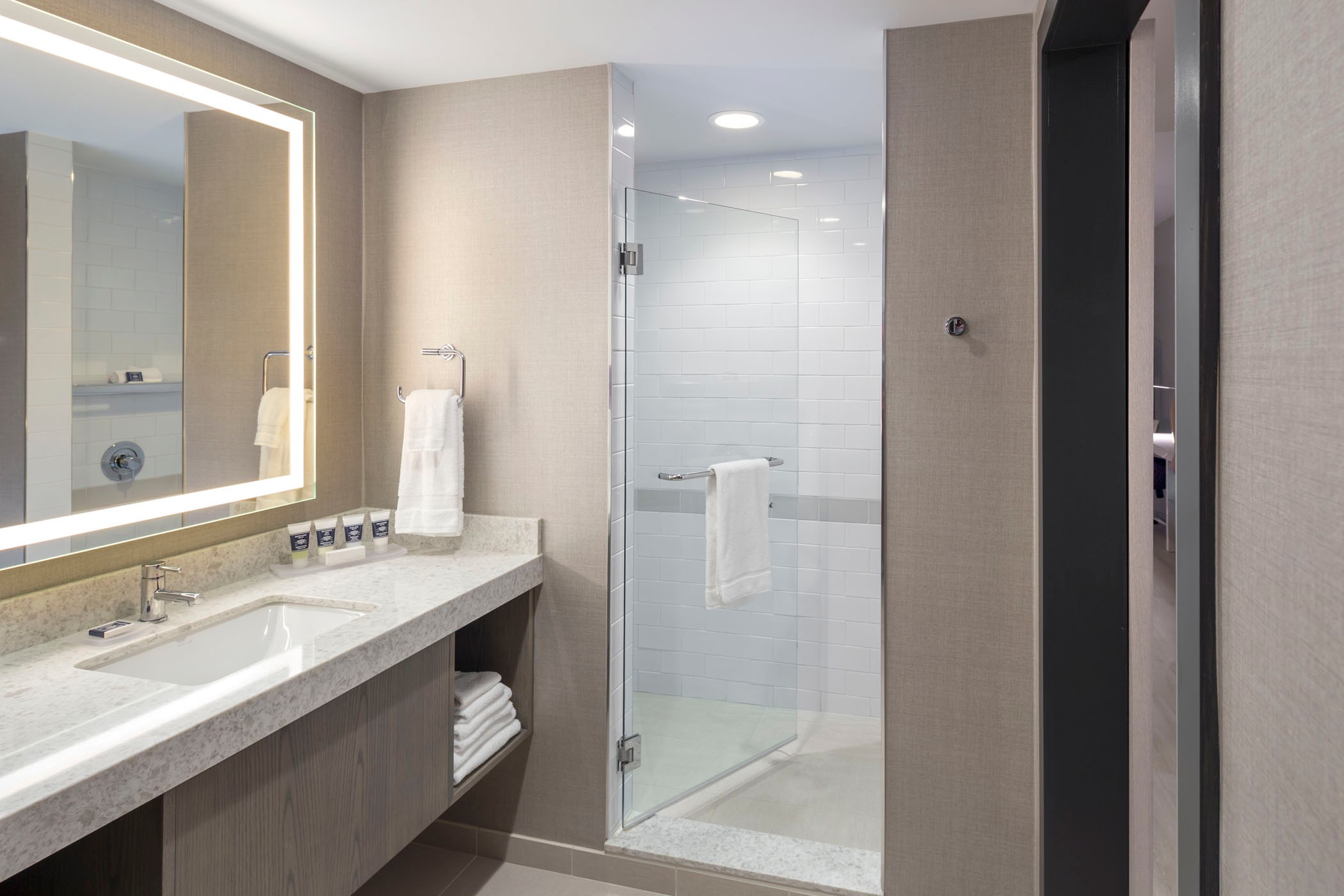 Modern bathroom with glass shower, illuminated mirror, and sleek countertop with toiletries.