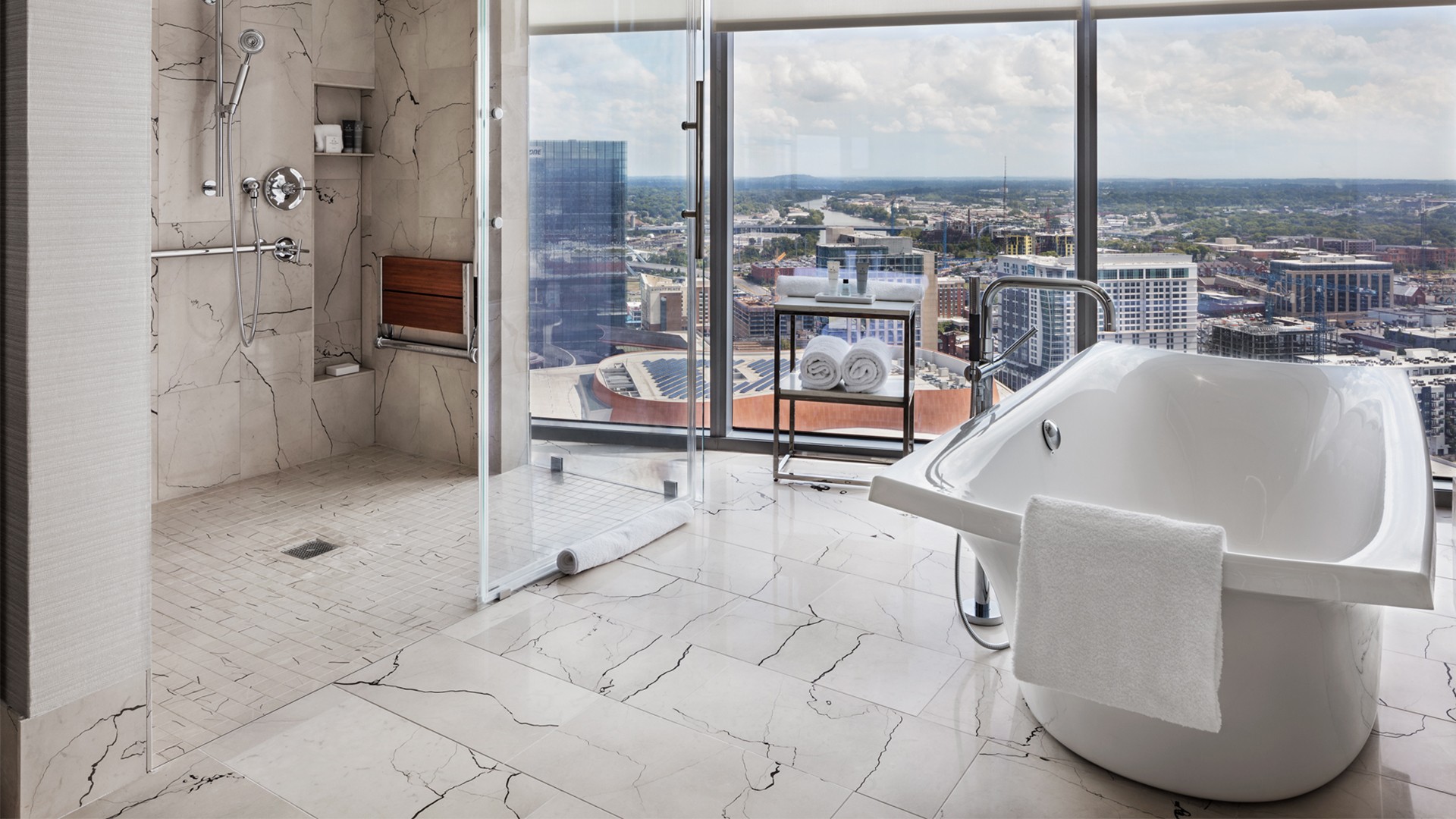 Modern bathroom with freestanding bathtub, glass shower, and city skyline view.