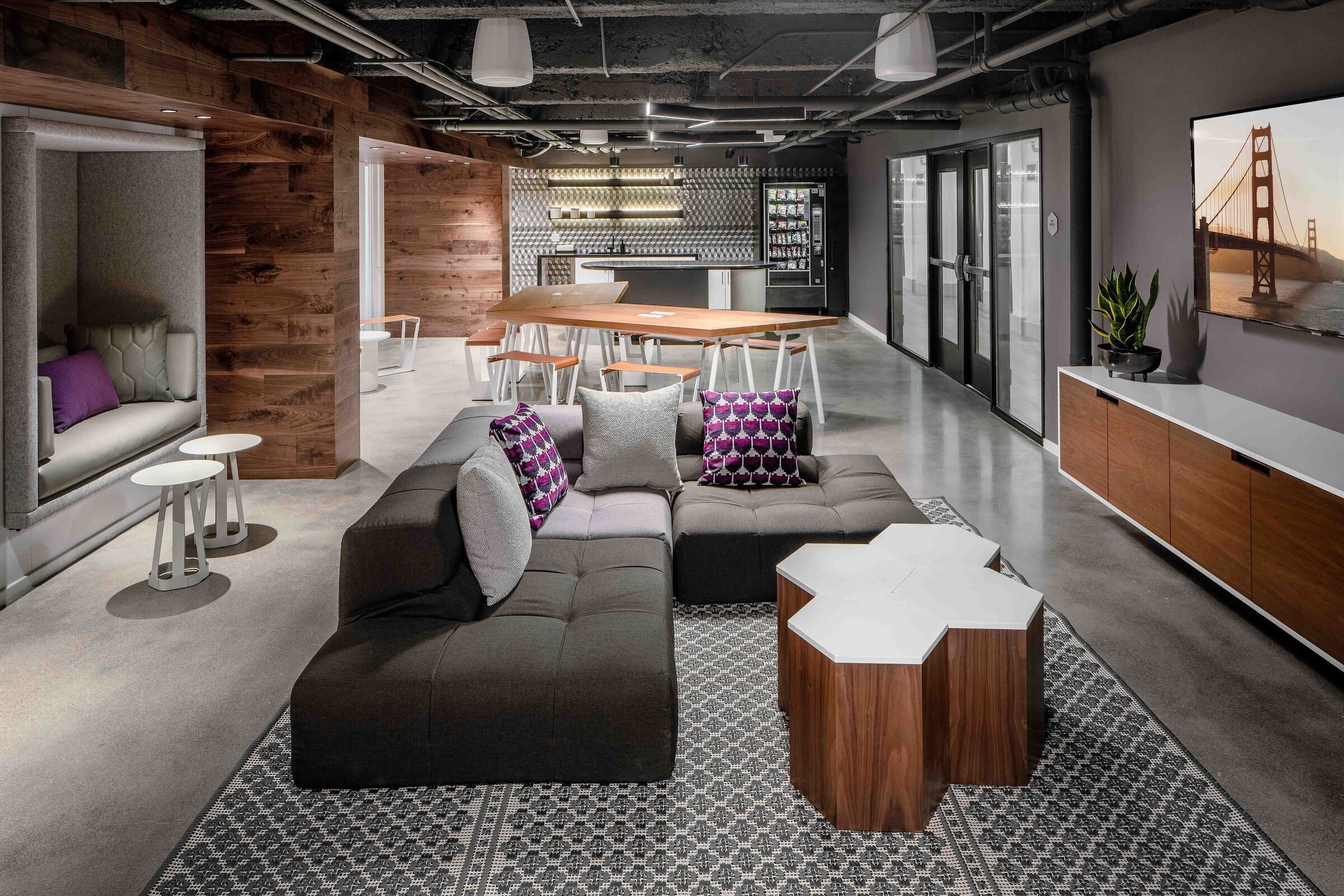 Modern office lounge with a sectional sofa, geometric tables, and a wall-mounted TV.