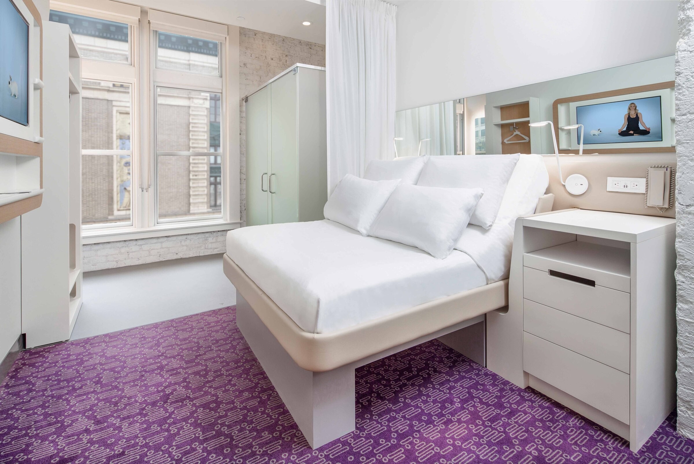 Moderner Hotelraum mit eleganter Einrichtung, einem lila gemusterten Teppich und großen Fenstern.