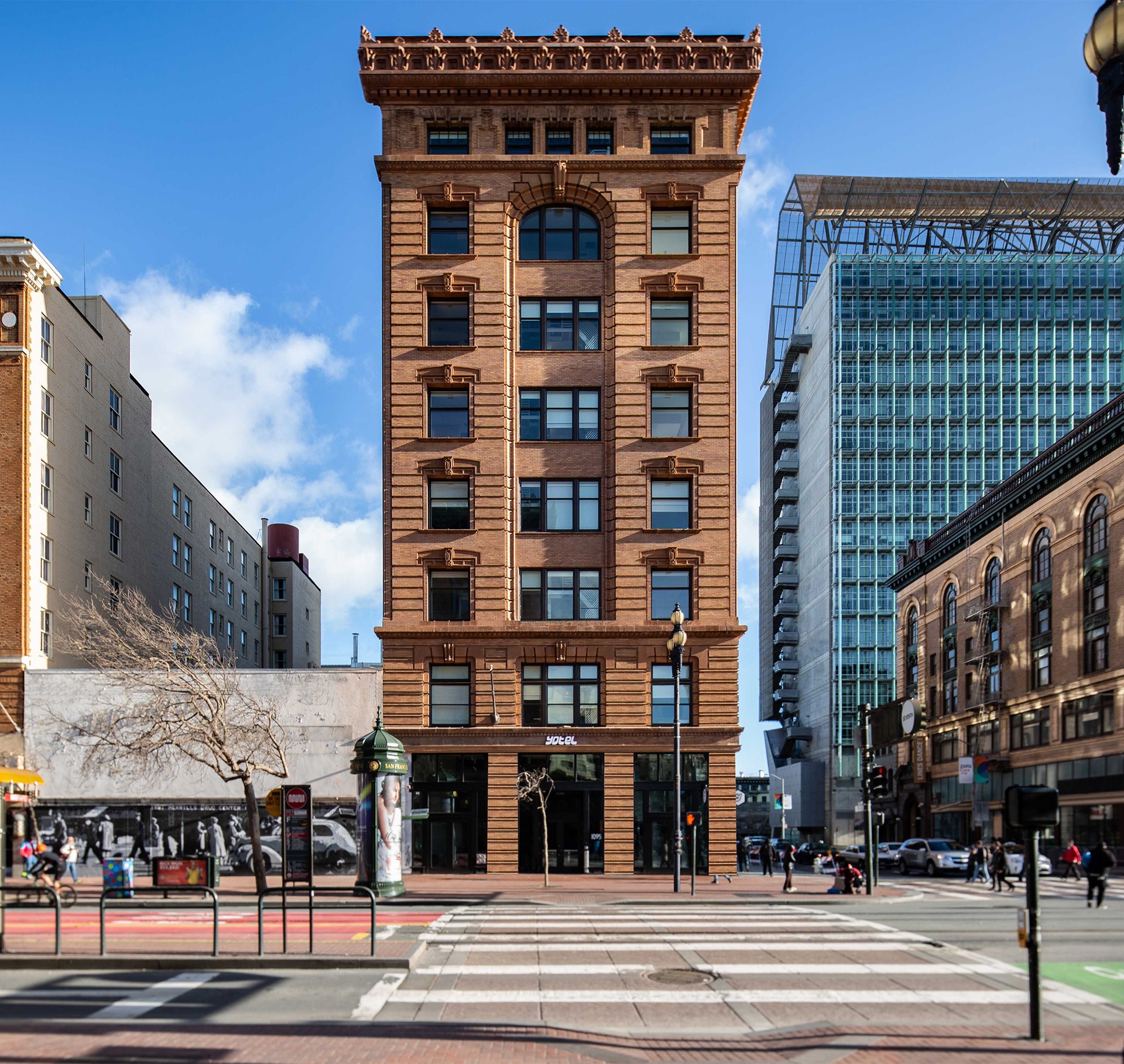 Historic red-brick building on a city corner under a clear blue sky, with street signs and taxi.