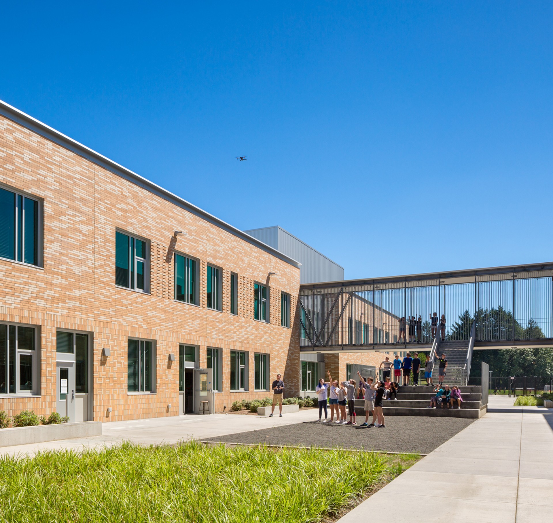 Modern School Courtyard with Students and Clear Blue Sky Modern school building with students outside under clear blue sky and a flying drone.