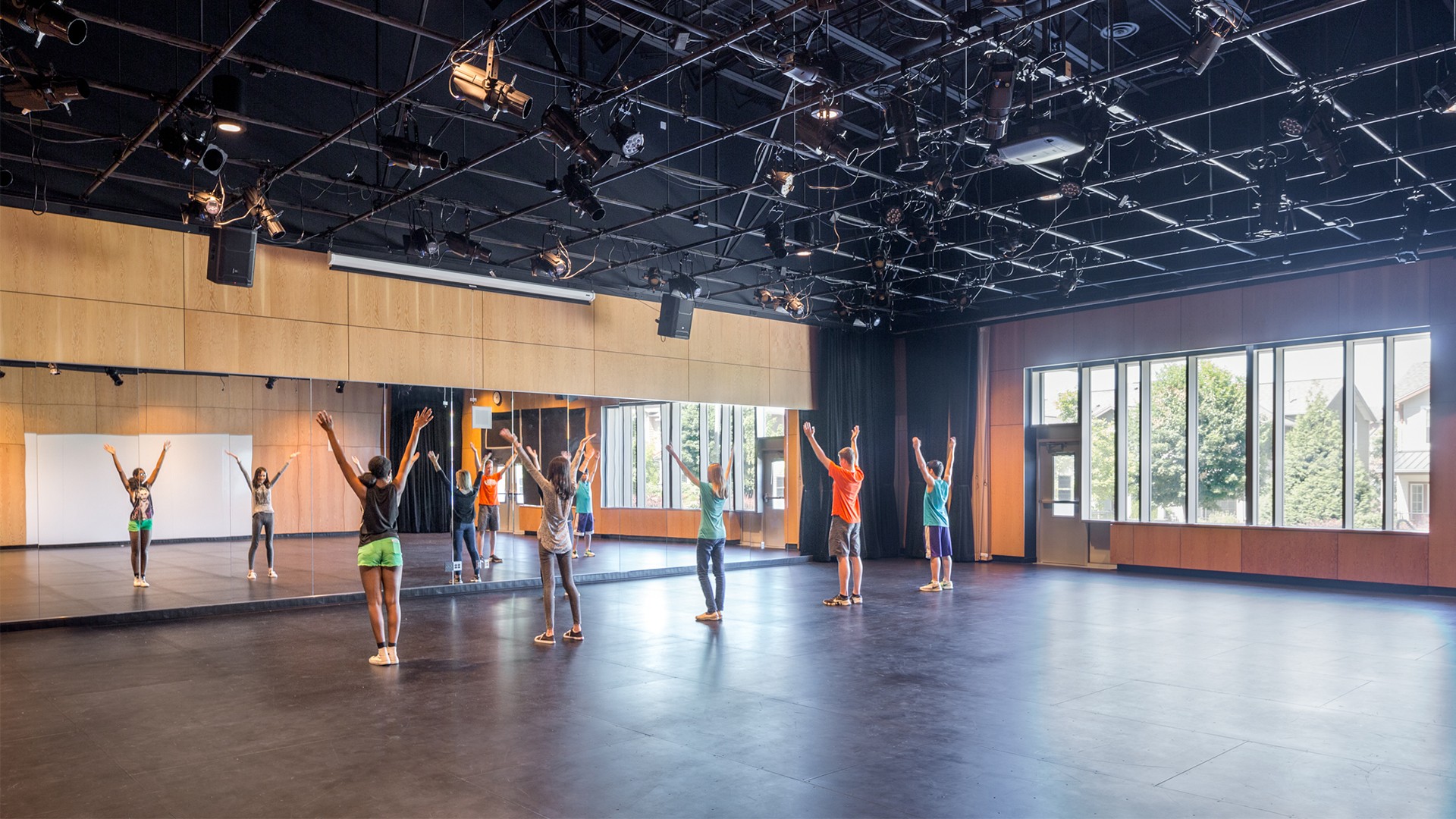 Children practicing dance moves in a spacious, well-lit studio with mirrors.