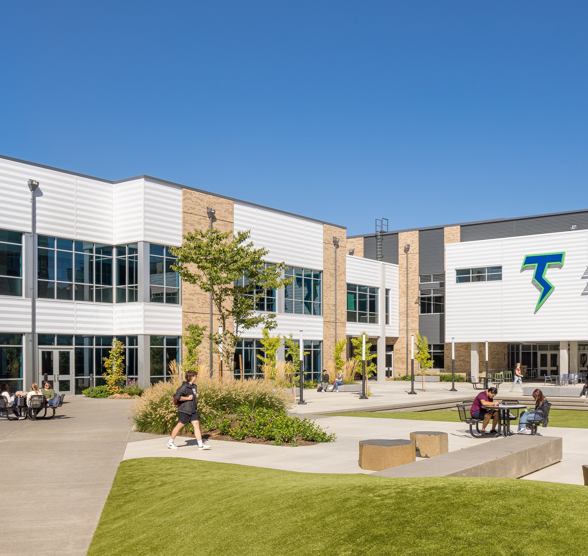 Modern School Campus Courtyard with Students and Greenery Modern school courtyard with students sitting and walking under clear blue sky.
