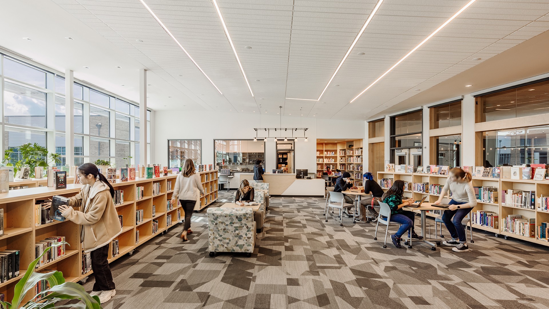 Bright modern library interior with people reading, browsing books, and studying.