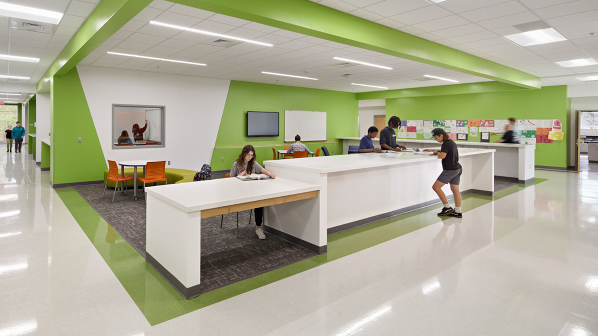 Modern school library with students studying at white tables and green accent walls.