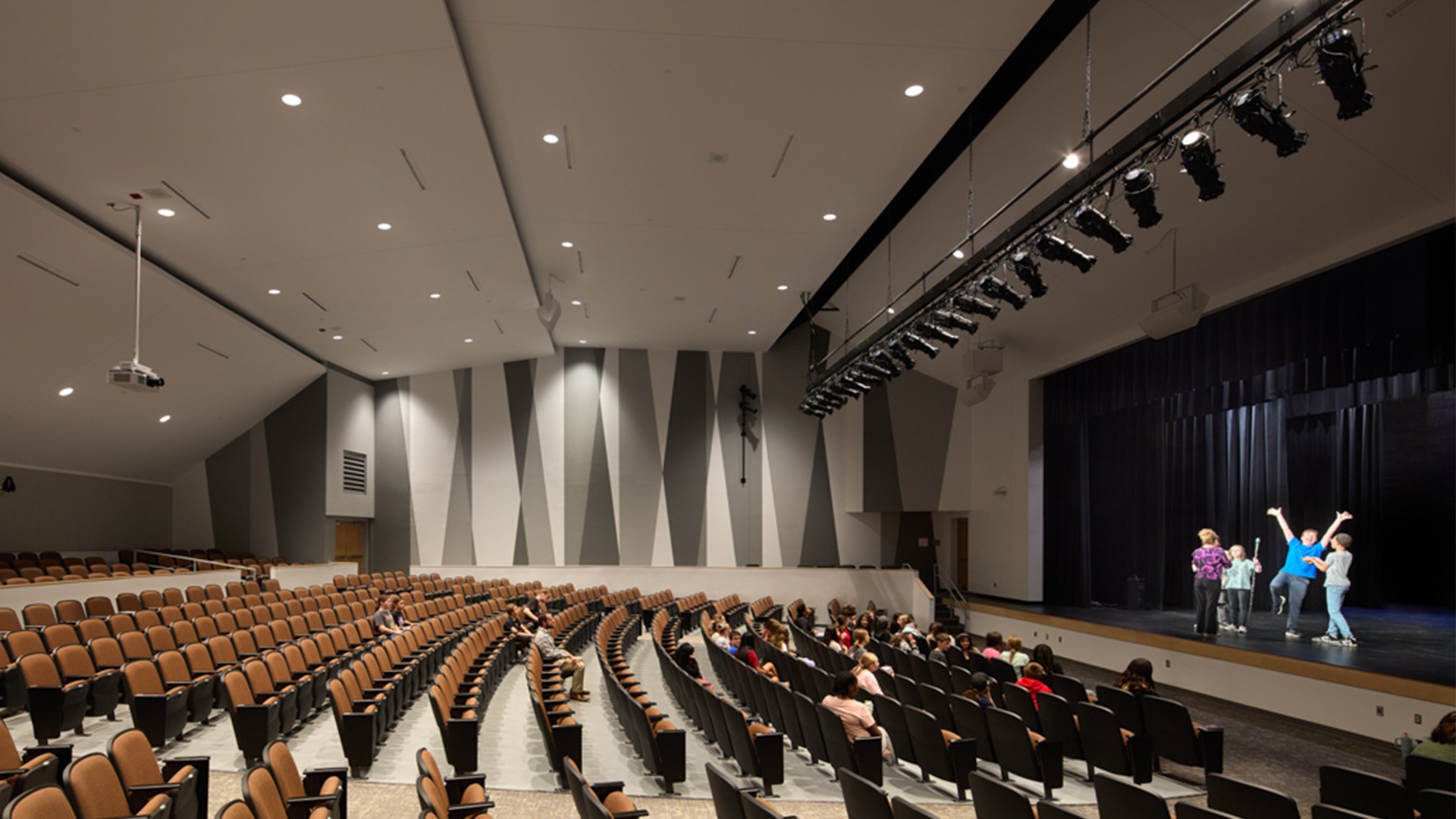 Audience watching a small group performing on stage in a modern auditorium.