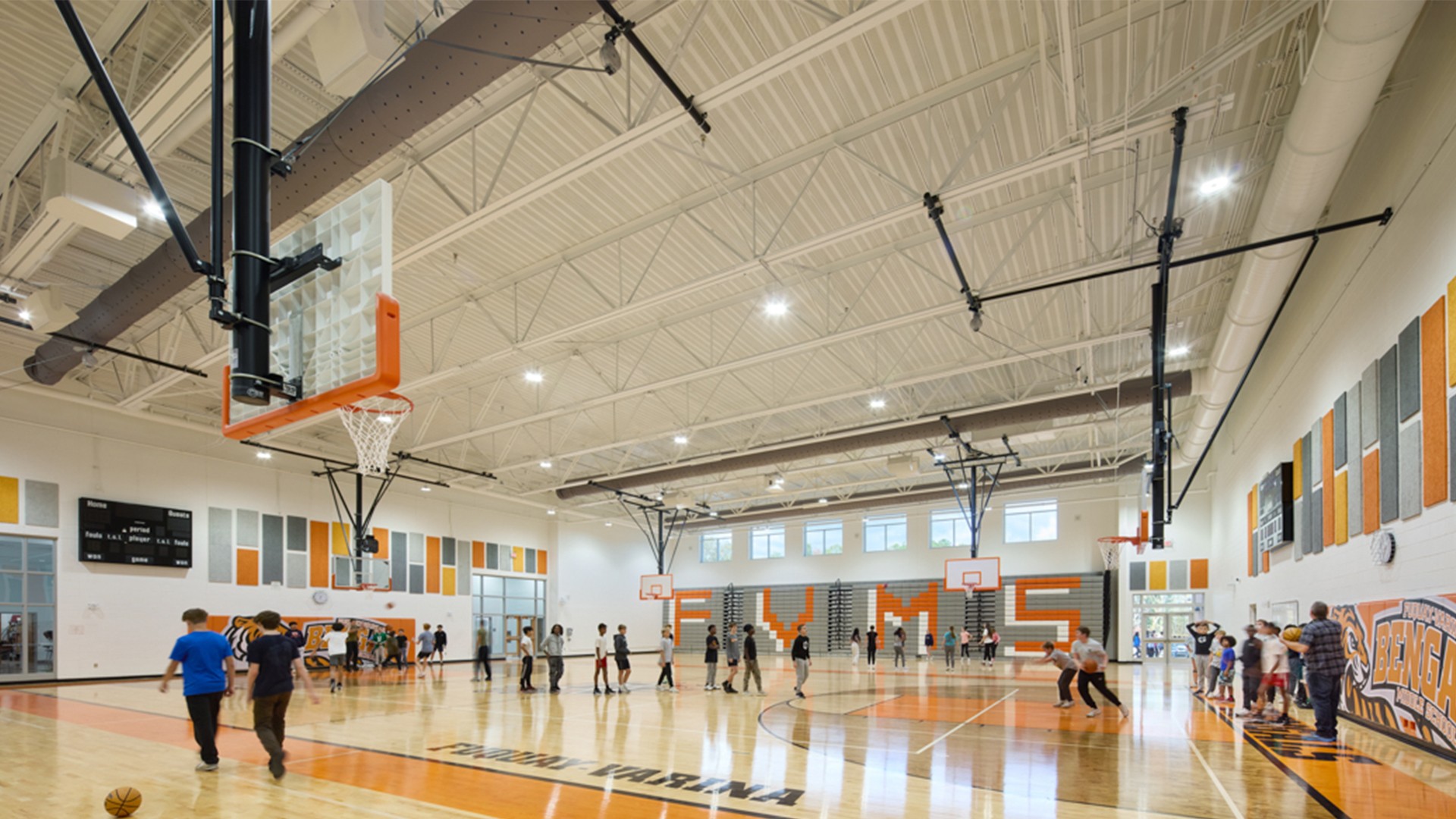 Indoor basketball court with children playing and bright overhead lighting.