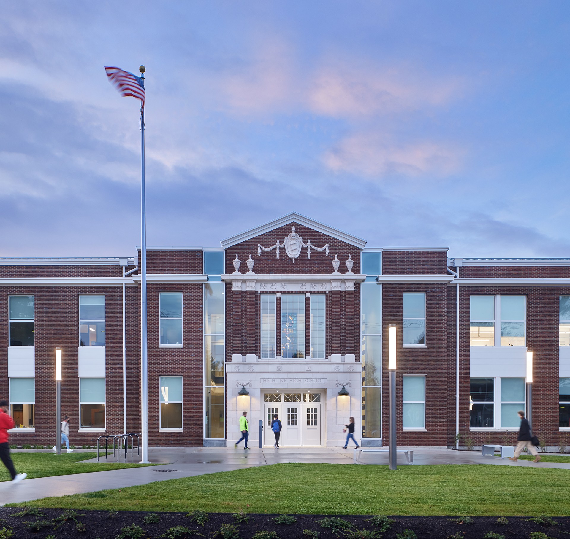 Modern School Building with American Flag at Sunset Front view of a modern brick school building with an American flag and students walking.